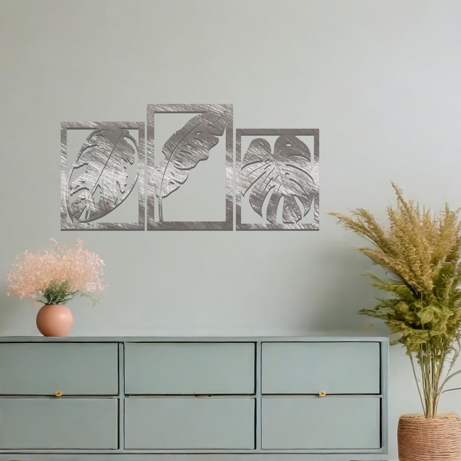 A metal wall art design featuring three leaf patterns, each in its own rectangular frame. The art is displayed on a neutral wall within a modern office space, enhancing the environment with its natural and minimalist appeal.