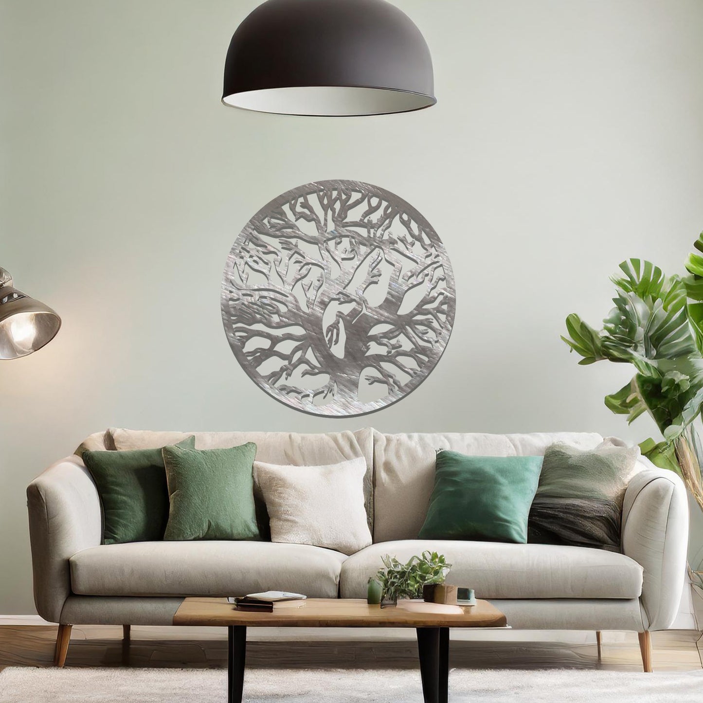 Metal wall art depicting a beautifully intricate tree design with twisting branches inside a circular frame. The artwork is placed on a neutral wall within a modern space, enhanced by the surrounding greenery and bookshelves.