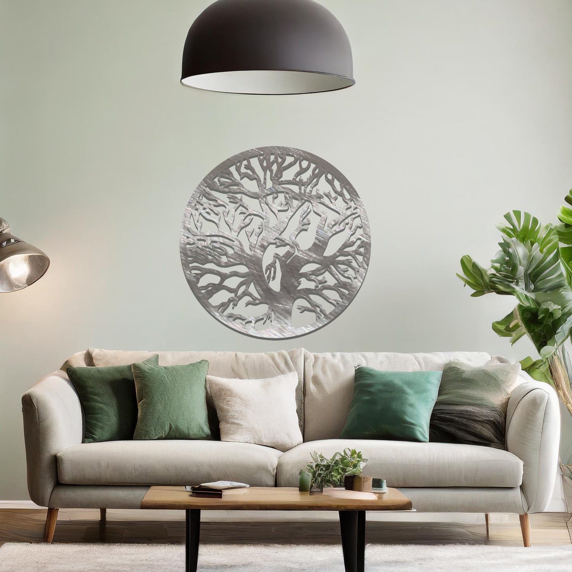 Metal wall art depicting a beautifully intricate tree design with twisting branches inside a circular frame. The artwork is placed on a neutral wall within a modern space, enhanced by the surrounding greenery and bookshelves.