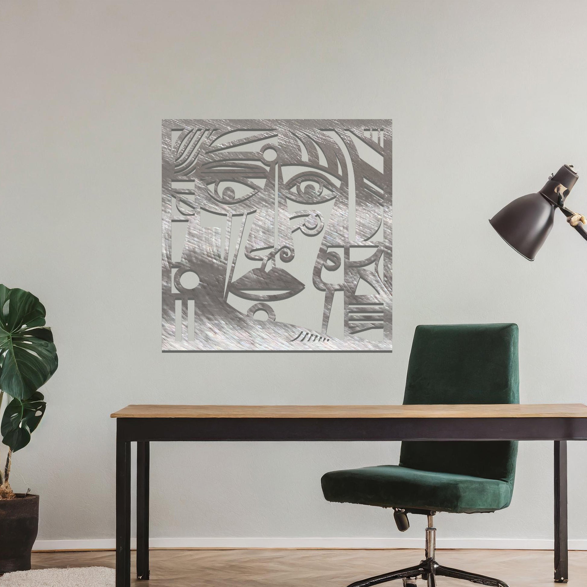 Geometric abstract face design cut from metal. The face features bold lines, sharp angles, and circular elements, creating a unique artistic representation. The art is displayed on a neutral wall in a modern room setting.