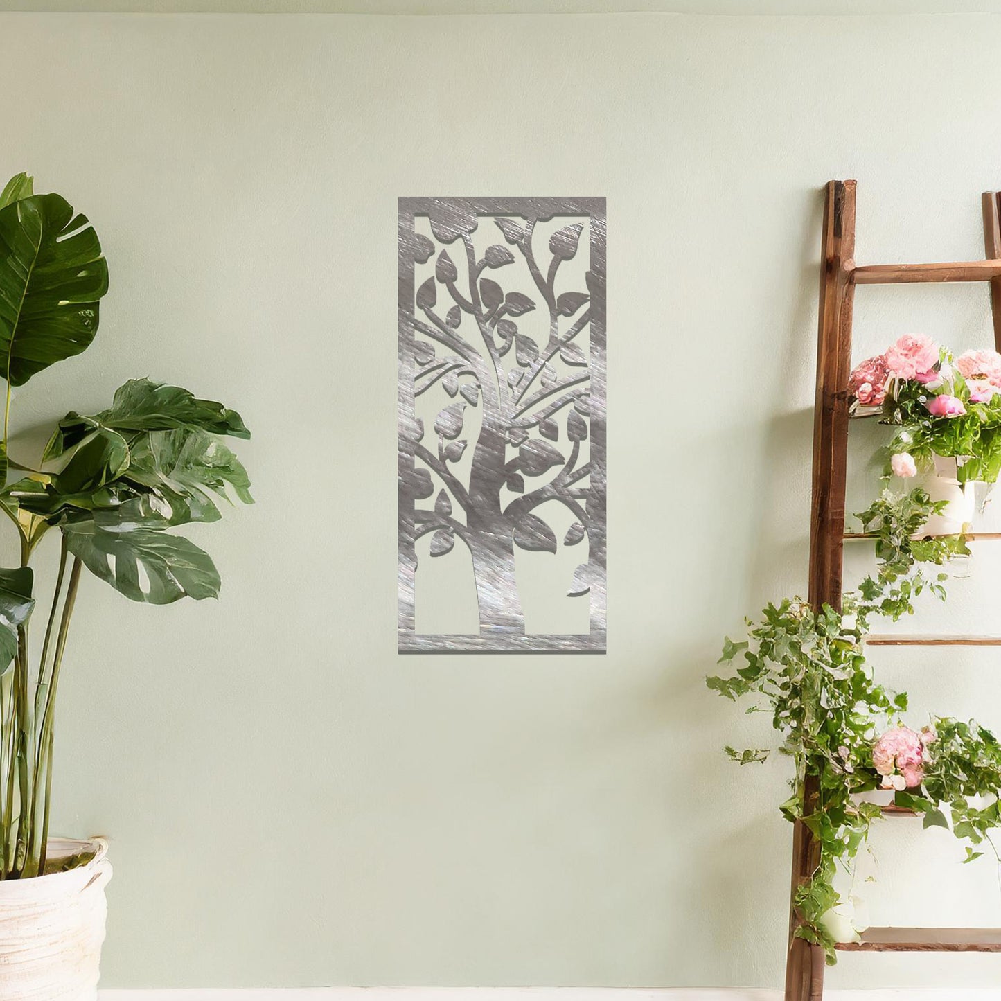 Metal wall art featuring a rectangular design with a stylised tree motif, showcasing flowing branches and leaves, mounted on a neutral wall within modern room decor. The minimalist craftsmanship adds a sleek and natural aesthetic, enhancing the contemporary elegance of the space.