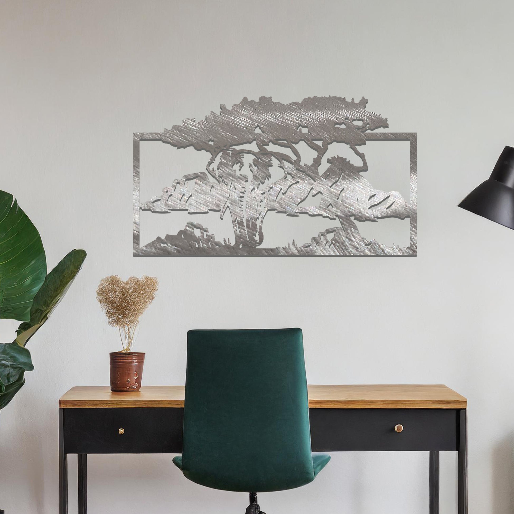 Metal wall art featuring an elephant silhouette under a tree with mountains in the background. The design is framed and placed on a neutral wall with contemporary furniture.