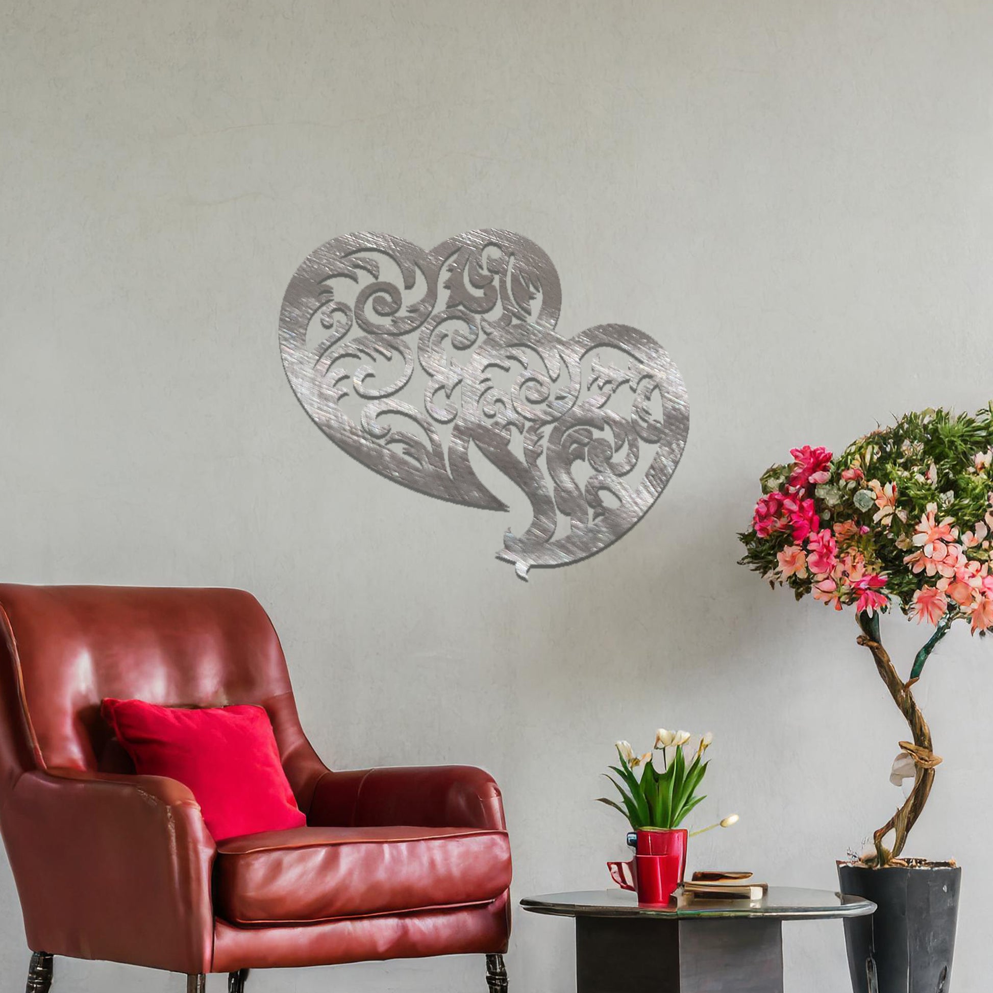 Metal wall art featuring a pair of intricately designed hearts with swirling patterns, mounted on a neutral wall within modern room decor. The elegant detailing creates a romantic and artistic focal point, adding a touch of love to the space.