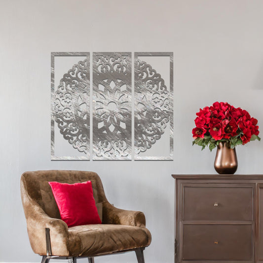 A metal wall art design split into three panels, featuring an intricate floral mandala pattern. The decorative piece is displayed on a neutral wall, adding an elegant, modern touch to the room's decor.