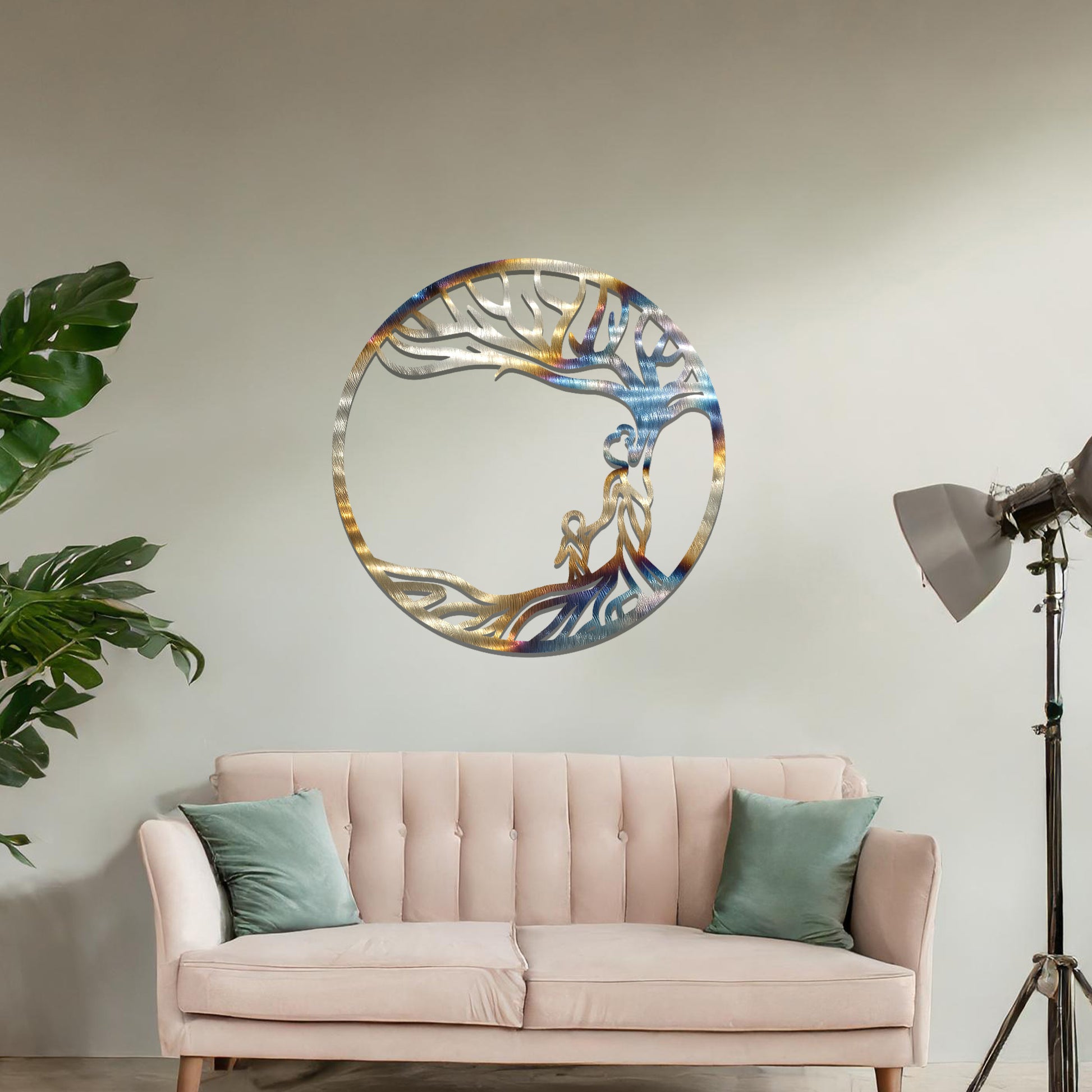 Metal wall art featuring a circular design with a symbolic tree and figures motif, depicting a parent and child under a tree with flowing branches, mounted on a neutral wall within modern room decor. The intricate design evokes warmth and connection, enhancing the aesthetic of the space.