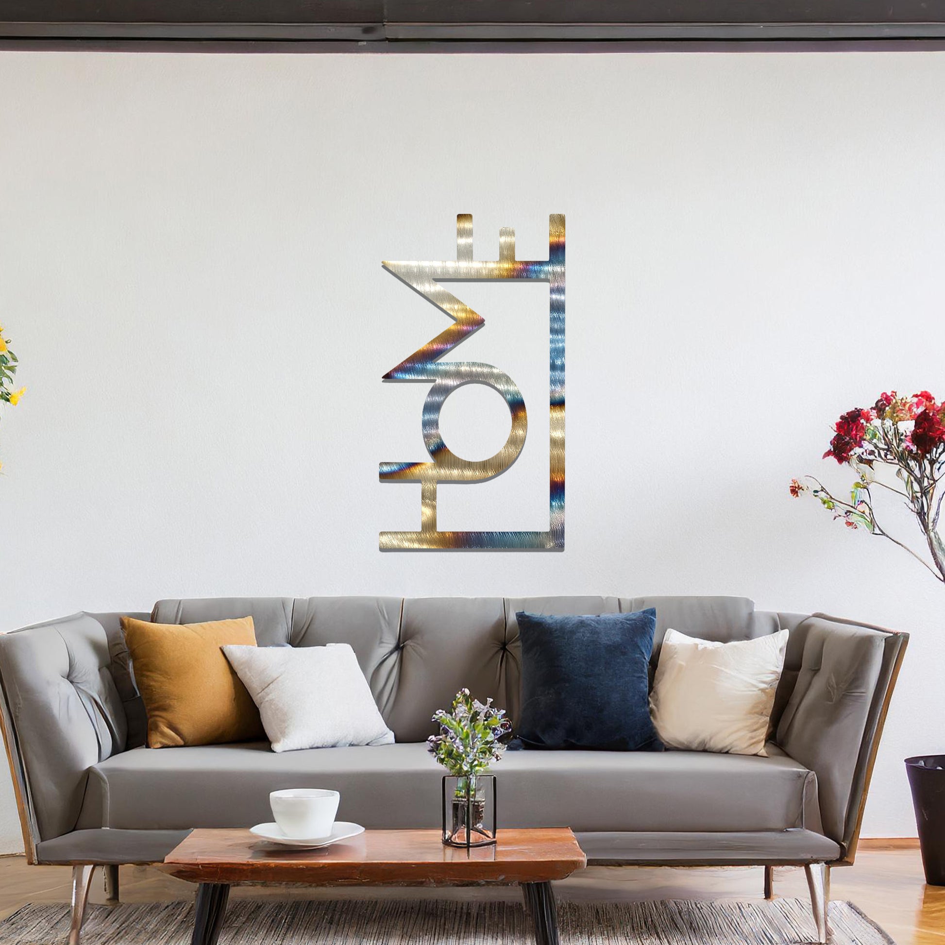 A modern metal wall art design featuring the word "HOME" in bold, geometric typography with an innovative, angular twist. The artwork is displayed on a neutral wall in a contemporary room setting.