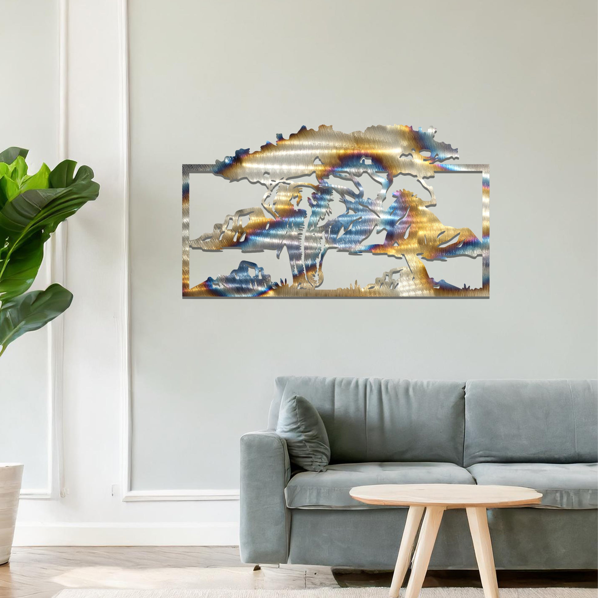 Metal wall art featuring an elephant silhouette under a tree with mountains in the background. The design is framed and placed on a neutral wall with contemporary furniture.