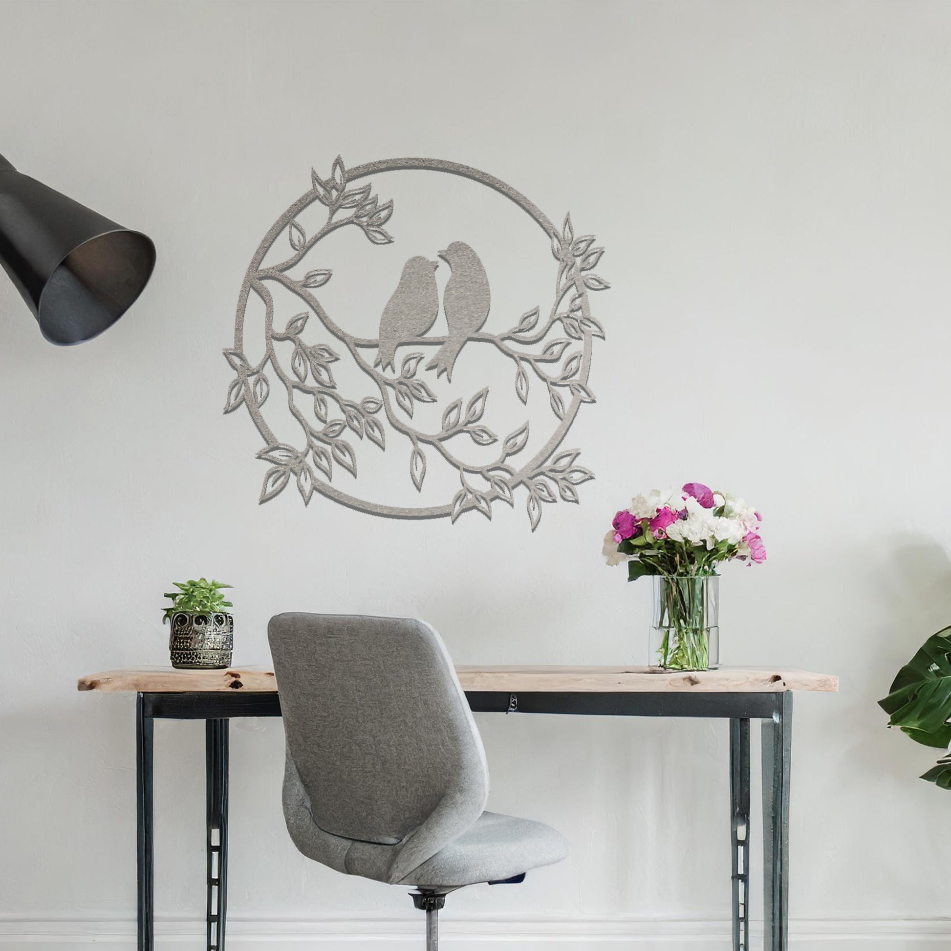Metal wall art featuring a circular design with two birds perched on a branch surrounded by intricate leaves, adding a charming focal point to a beautifully styled living space.