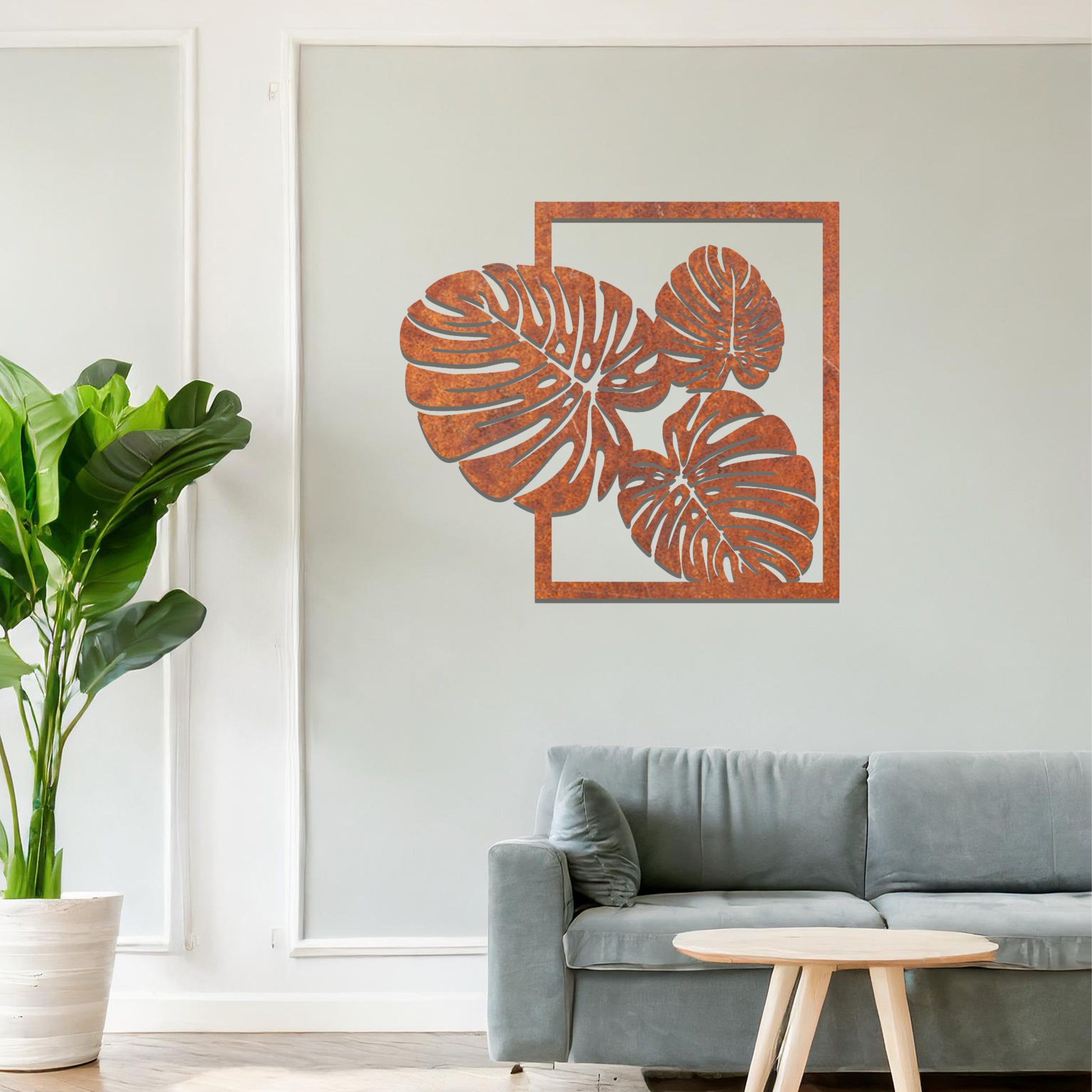 Metal wall art featuring a design of three large, detailed Monstera leaves arranged within a rectangular frame. The intricate cut-out pattern highlights the natural lines and veins of the leaves. The artwork is displayed against a neutral wall in a modern setting.