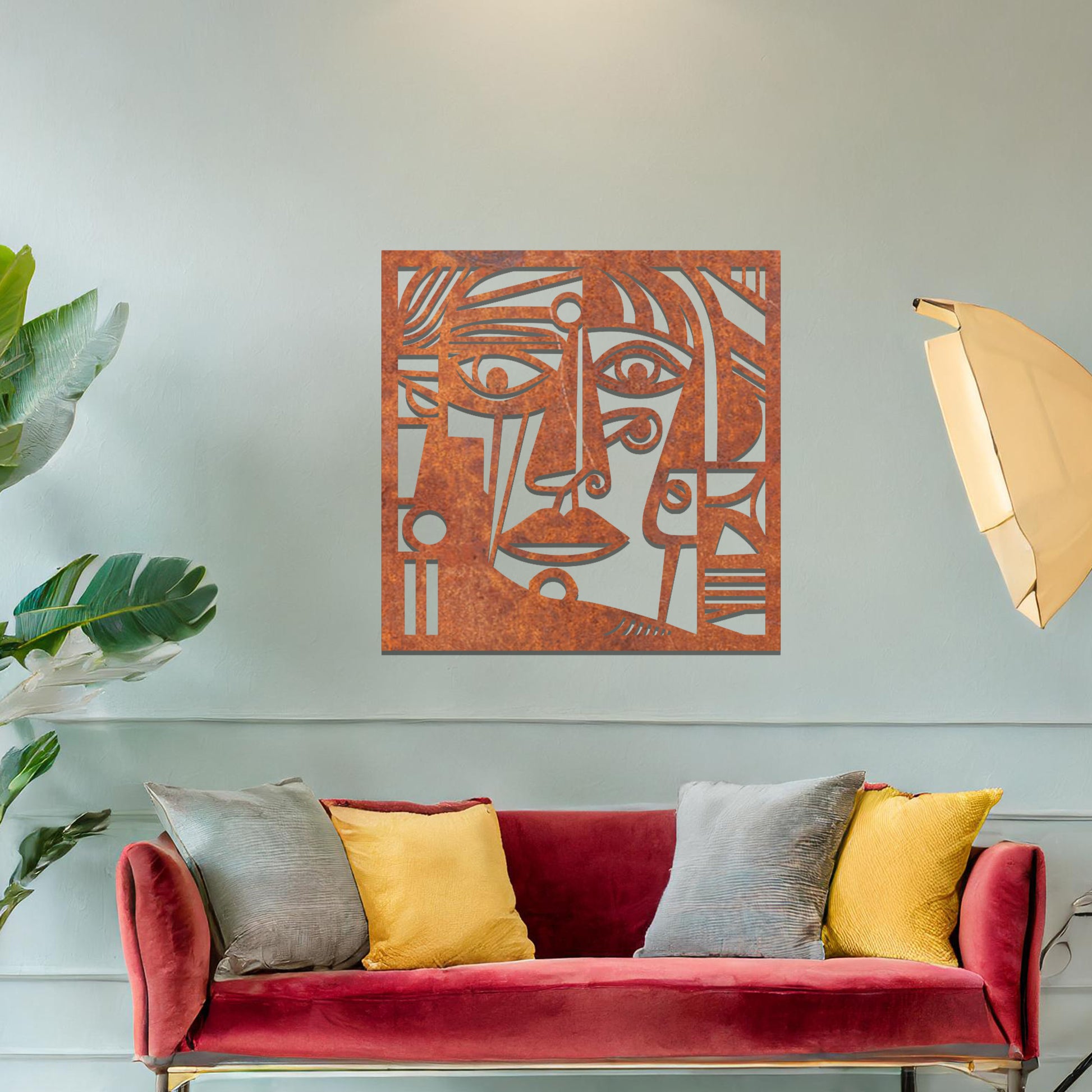 Geometric abstract face design cut from metal. The face features bold lines, sharp angles, and circular elements, creating a unique artistic representation. The art is displayed on a neutral wall in a modern room setting.