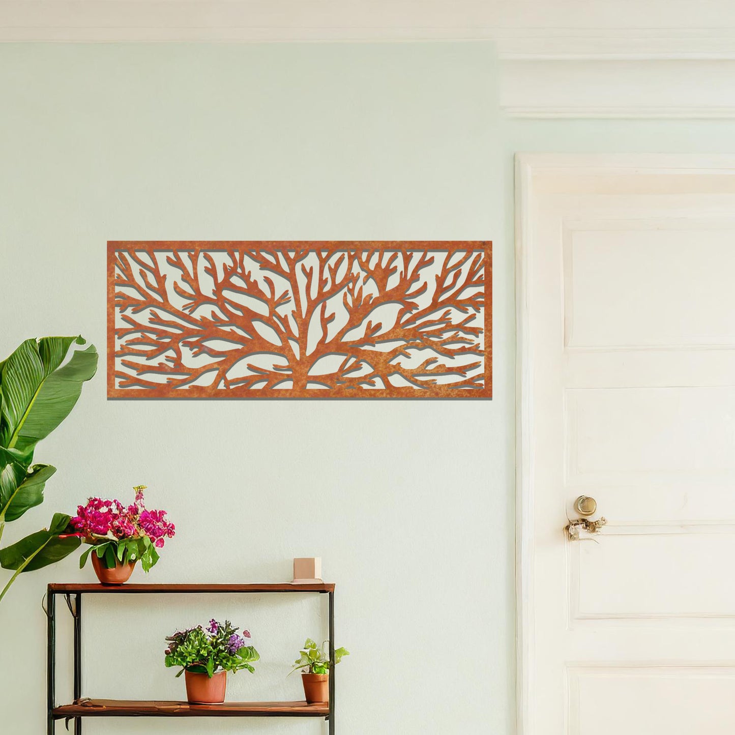 A metal wall art design featuring a detailed tree silhouette with sprawling branches, enclosed in a rectangular frame. The art is displayed on a neutral wall in a modern living room, complementing the contemporary decor and natural elements in the space.