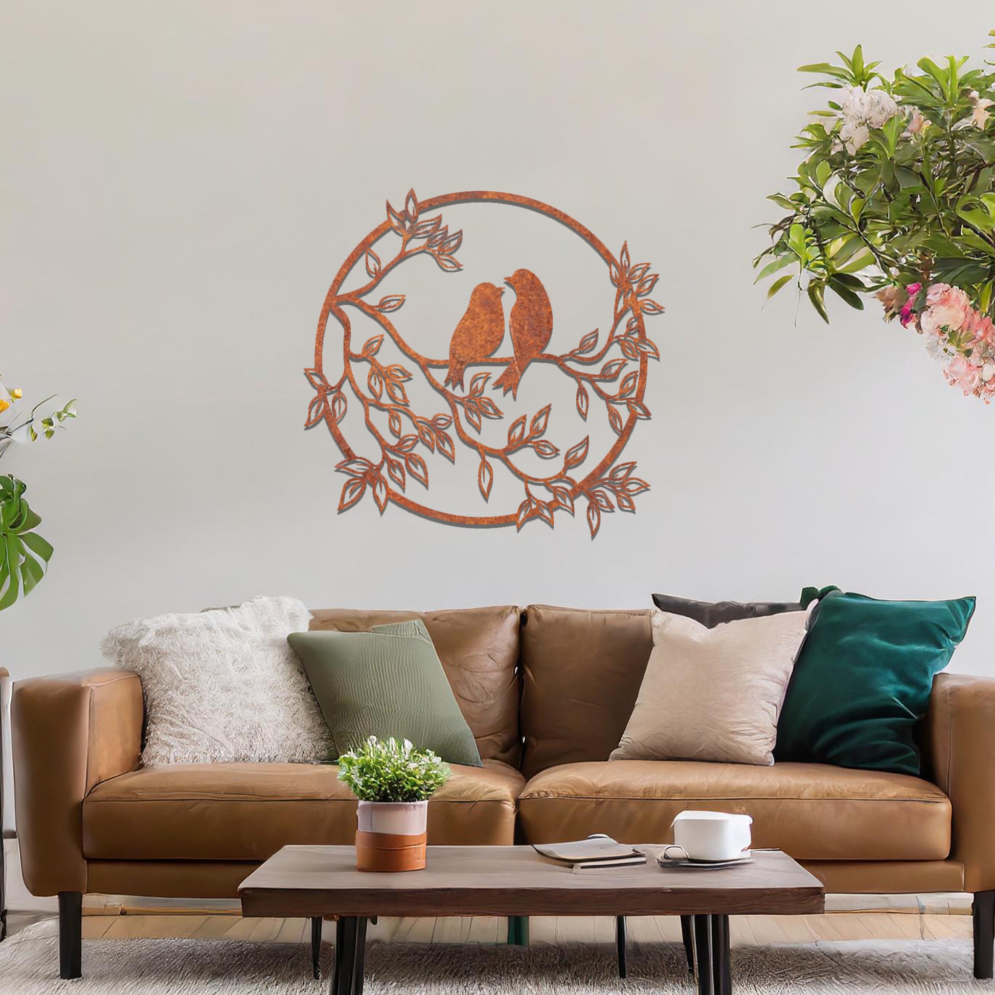 Metal wall art featuring a circular design with two birds perched on a branch surrounded by intricate leaves, adding a charming focal point to a beautifully styled living space.