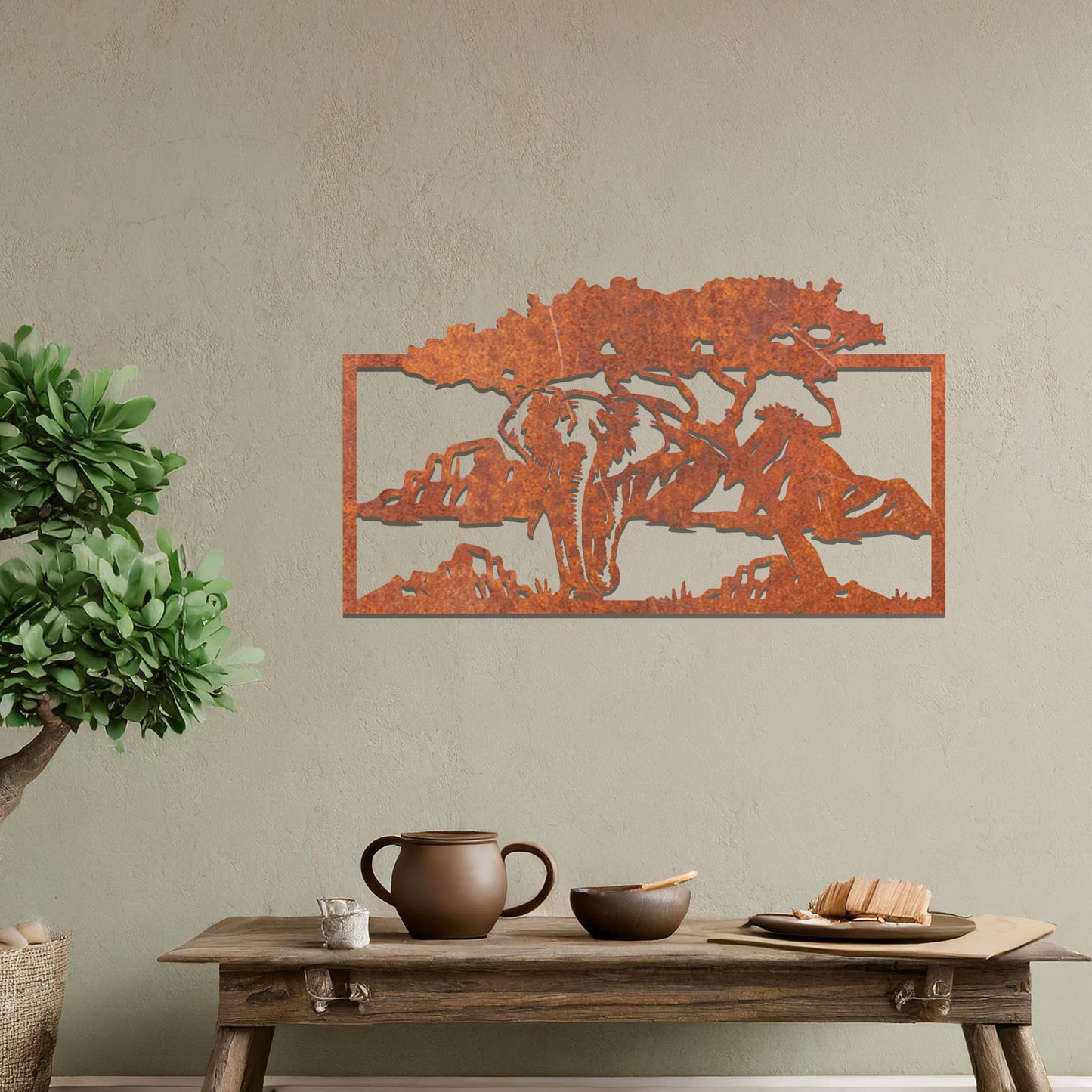 Metal wall art featuring an elephant silhouette under a tree with mountains in the background. The design is framed and placed on a neutral wall with contemporary furniture.