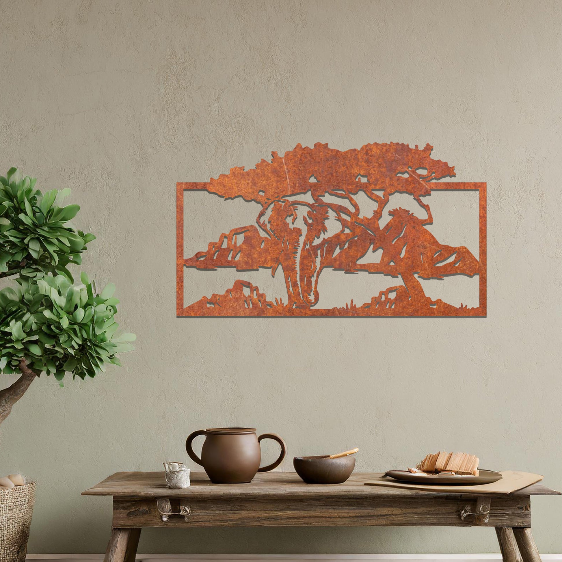 Metal wall art featuring an elephant silhouette under a tree with mountains in the background. The design is framed and placed on a neutral wall with contemporary furniture.