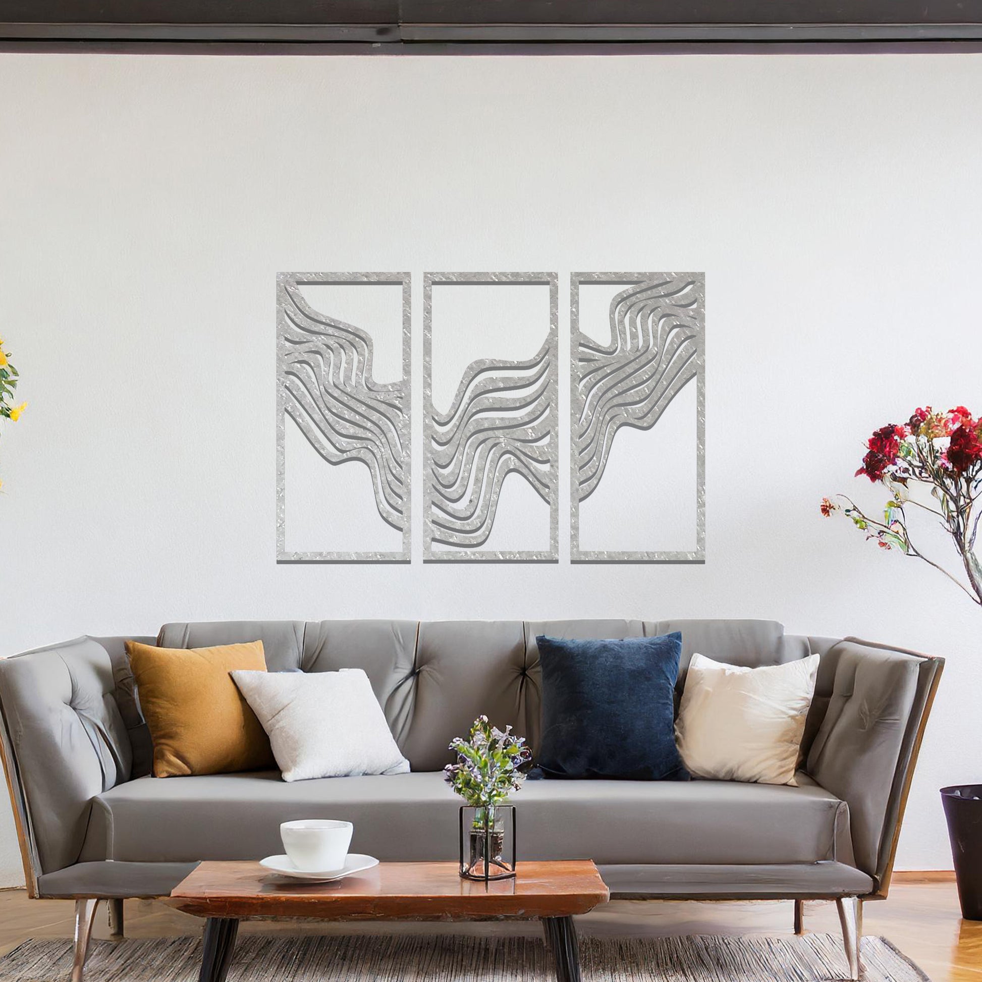 Metal wall art set of three panels featuring flowing, wave-like patterns. The design flows across the panels with a smooth, dynamic movement. The art is placed on a neutral wall in a modern living room, enhancing the space with a sleek, contemporary feel.