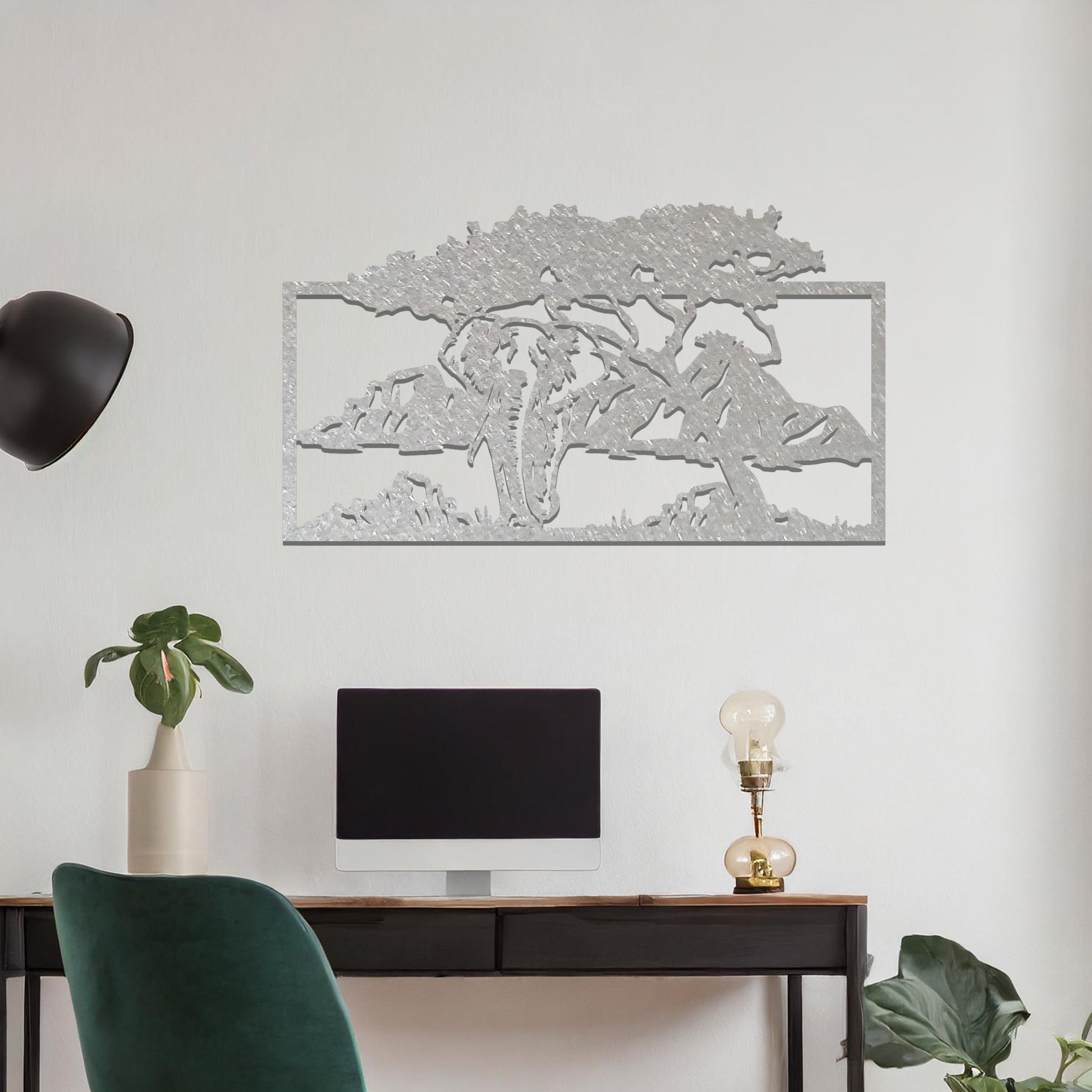 Metal wall art featuring an elephant silhouette under a tree with mountains in the background. The design is framed and placed on a neutral wall with contemporary furniture.