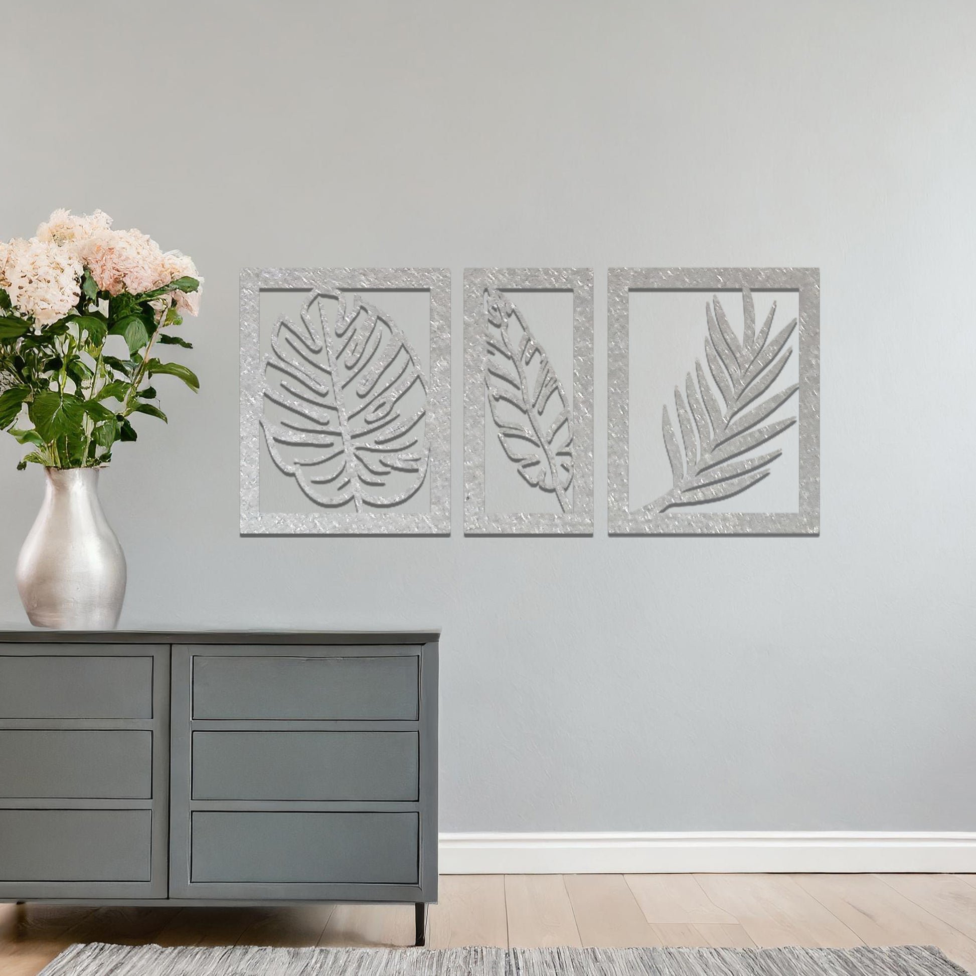 Metal wall art featuring a three-panel design with detailed leaf patterns, mounted on a neutral wall within modern decor. The organic motifs and rust finish create a natural, earthy focal point, enhancing the room's aesthetic.