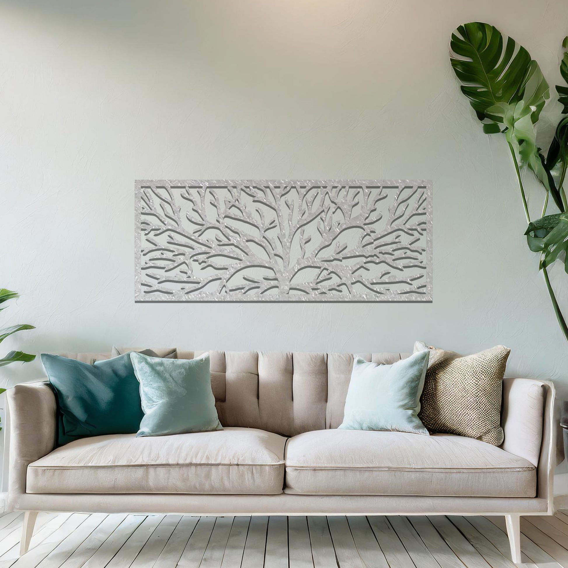 A metal wall art design featuring a detailed tree silhouette with sprawling branches, enclosed in a rectangular frame. The art is displayed on a neutral wall in a modern living room, complementing the contemporary decor and natural elements in the space.