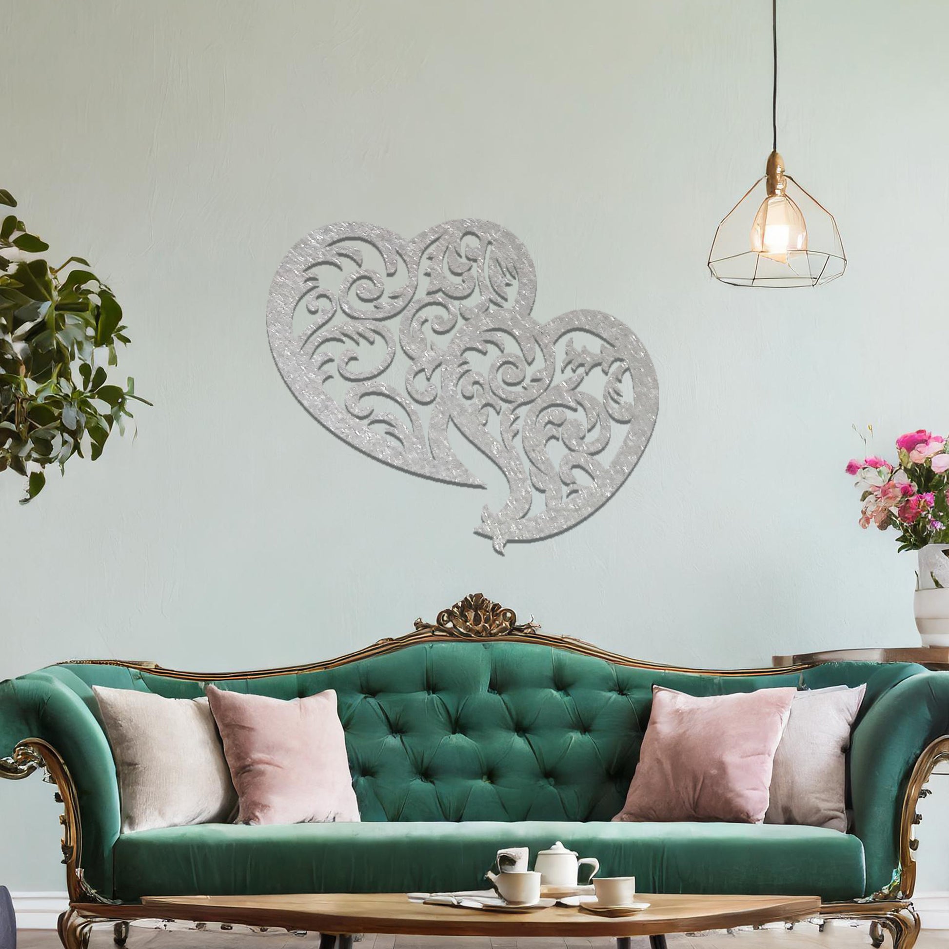 Metal wall art featuring a pair of intricately designed hearts with swirling patterns, mounted on a neutral wall within modern room decor. The elegant detailing creates a romantic and artistic focal point, adding a touch of love to the space.