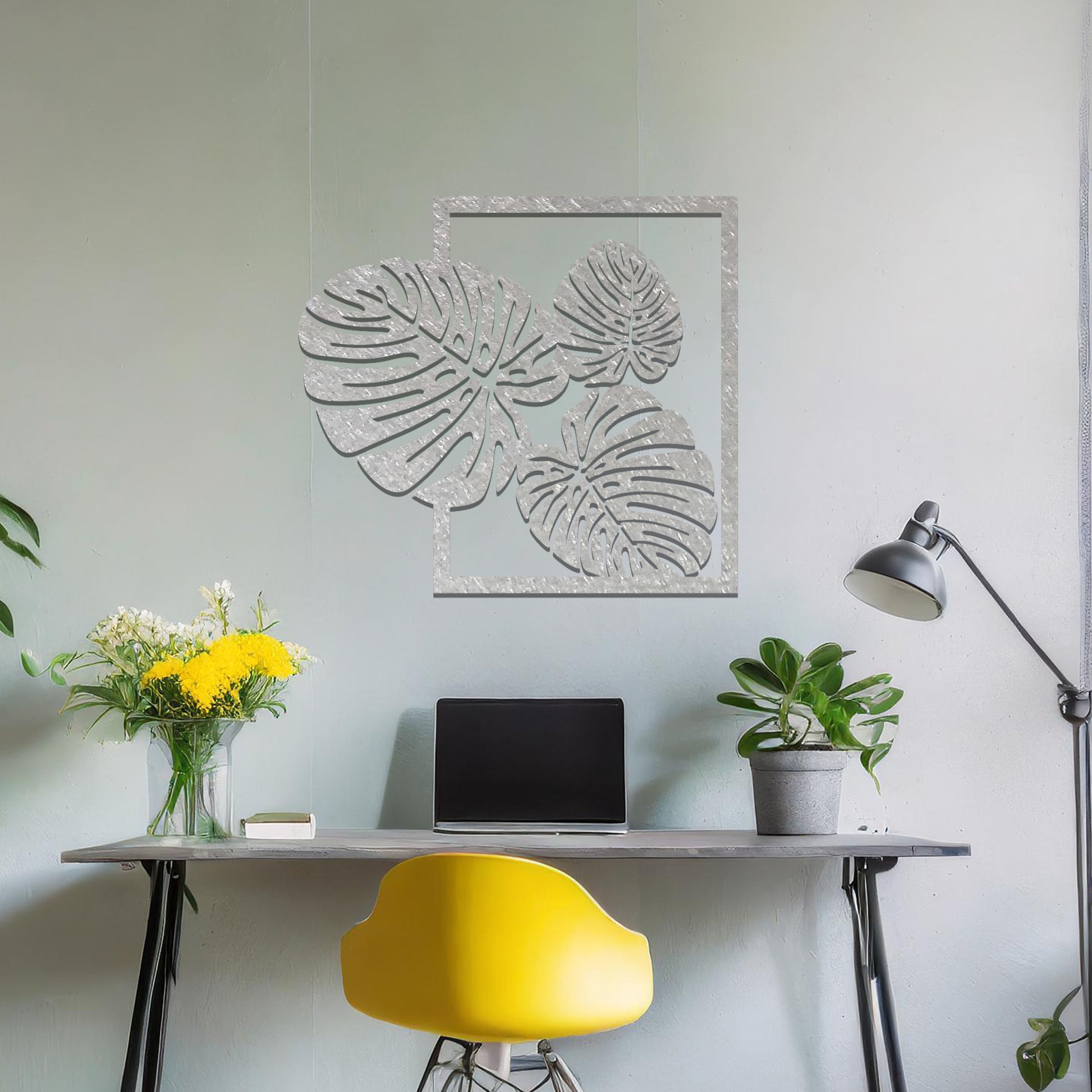 Metal wall art featuring a design of three large, detailed Monstera leaves arranged within a rectangular frame. The intricate cut-out pattern highlights the natural lines and veins of the leaves. The artwork is displayed against a neutral wall in a modern setting.