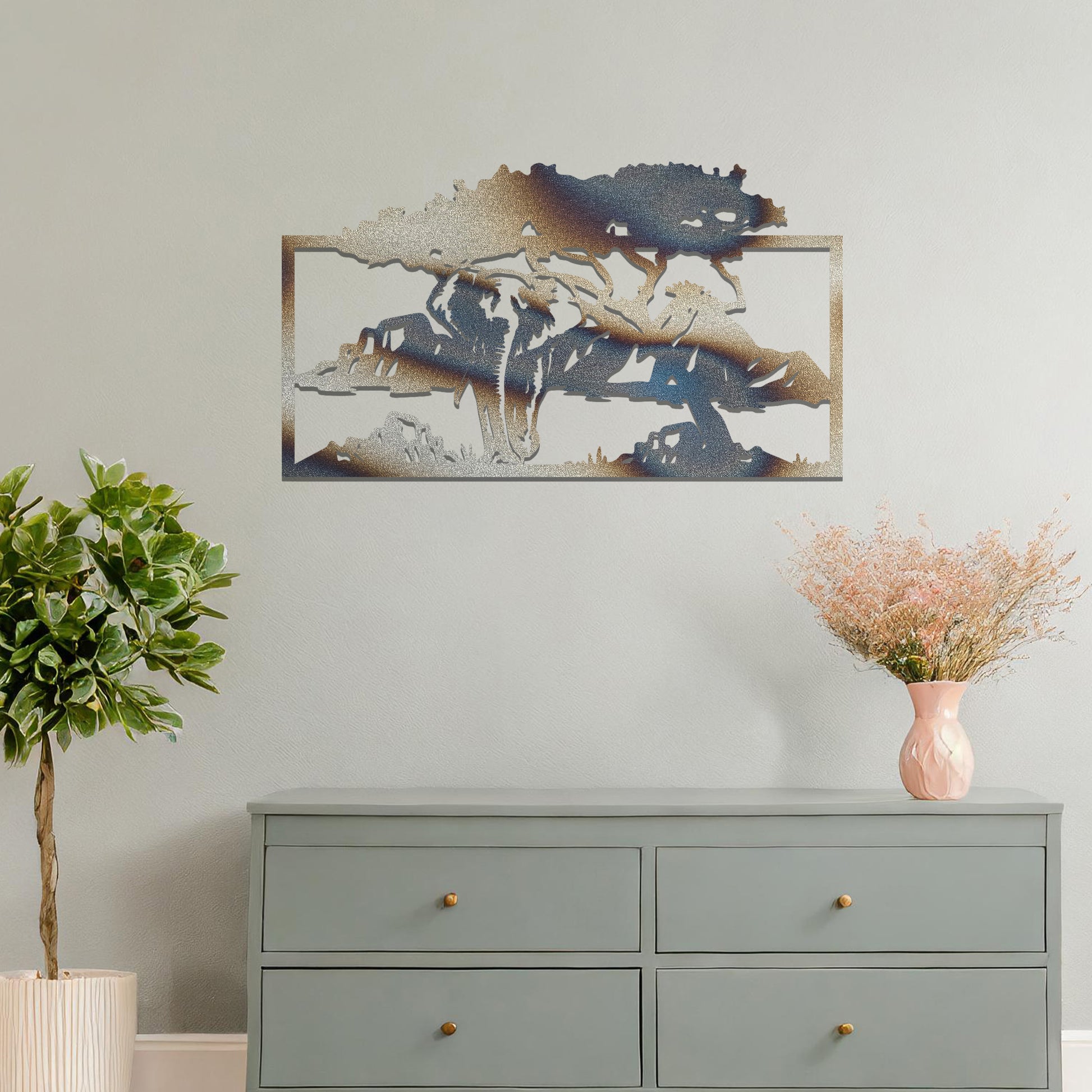 Metal wall art featuring an elephant silhouette under a tree with mountains in the background. The design is framed and placed on a neutral wall with contemporary furniture.