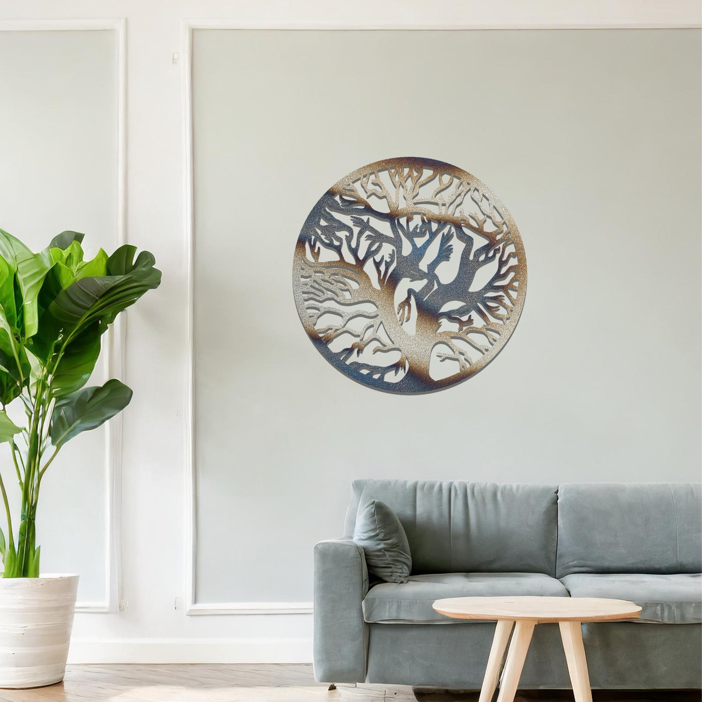 Metal wall art depicting a beautifully intricate tree design with twisting branches inside a circular frame. The artwork is placed on a neutral wall within a modern space, enhanced by the surrounding greenery and bookshelves.