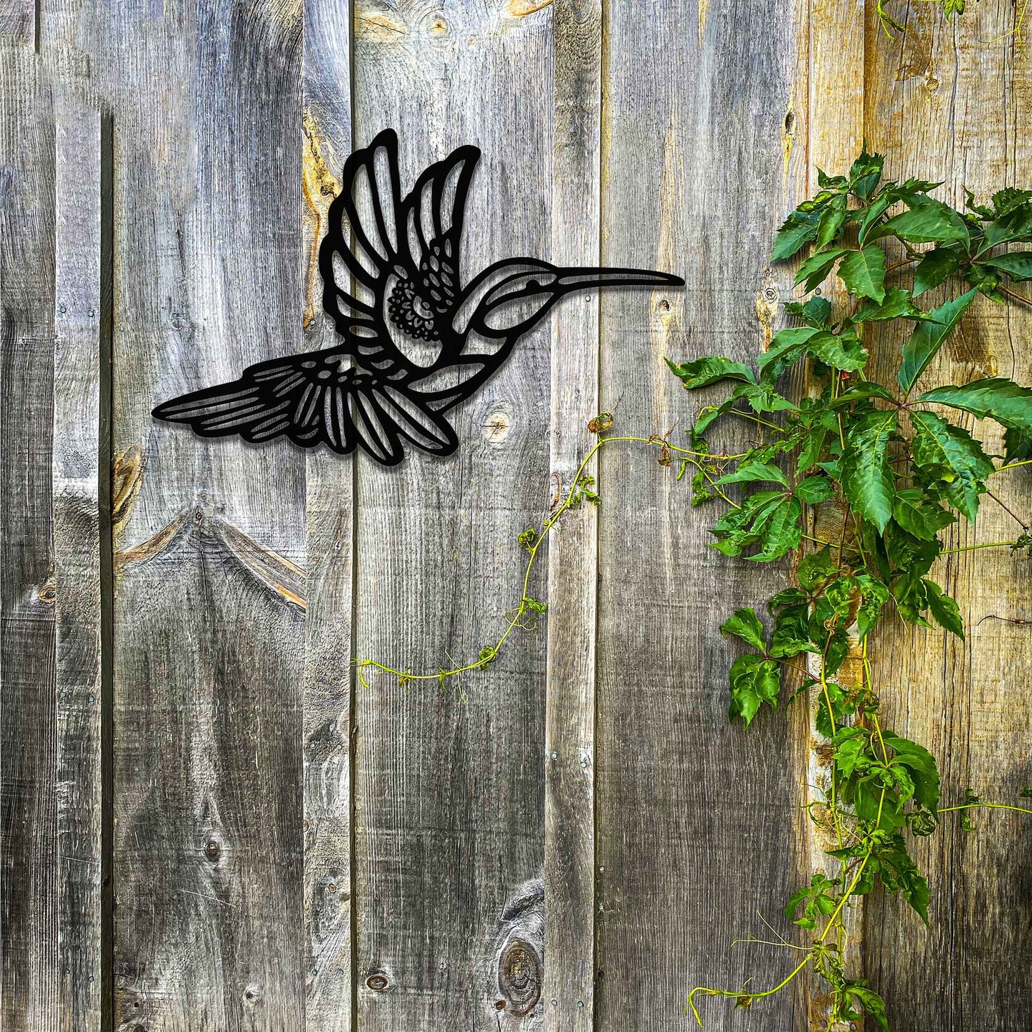 Metal garden decoration featuring a hummingbird in flight with intricate detailing, showcasing a rustic finish that adds a natural and artistic charm to outdoor walls or garden settings.