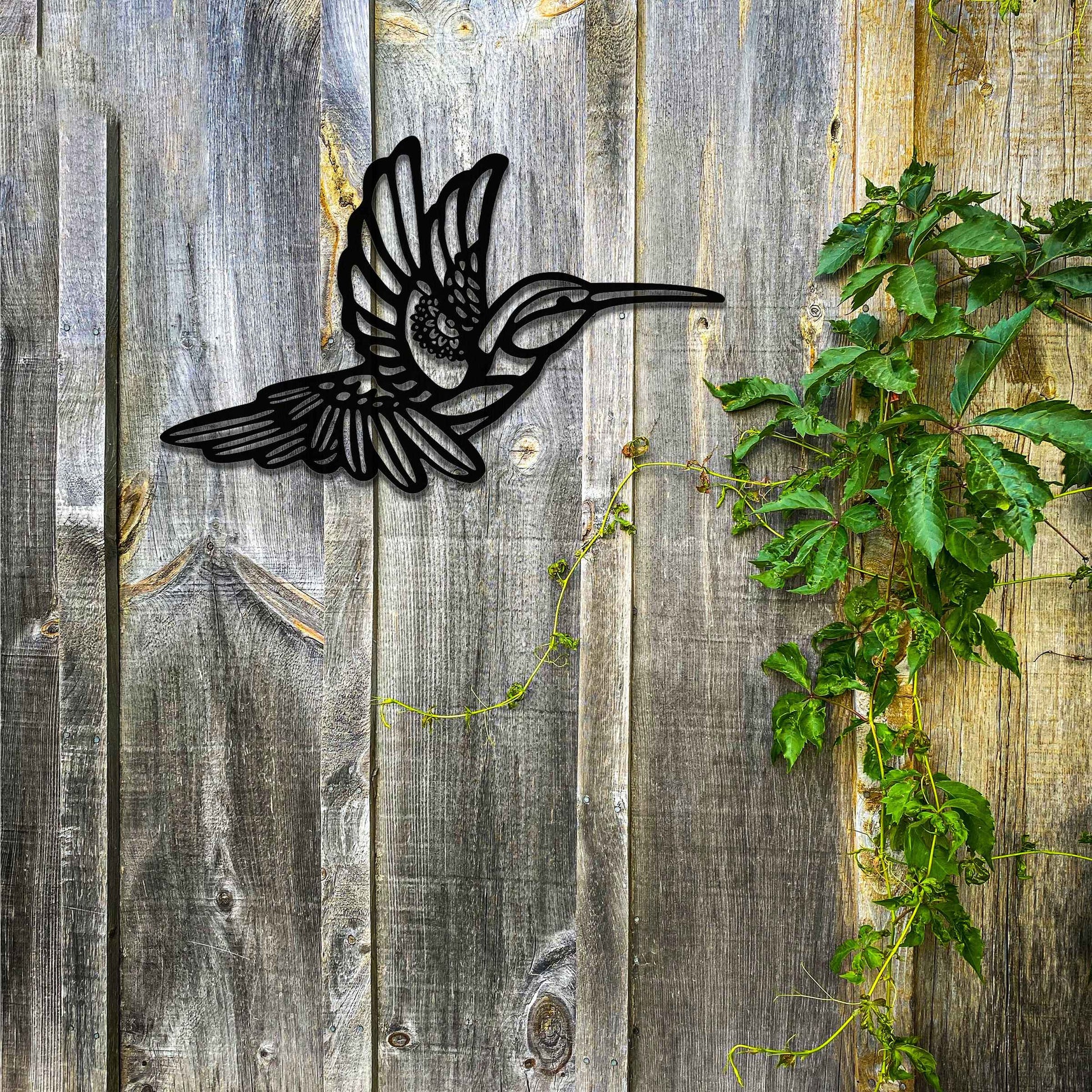 Metal garden decoration featuring a hummingbird in flight with intricate detailing, showcasing a rustic finish that adds a natural and artistic charm to outdoor walls or garden settings.