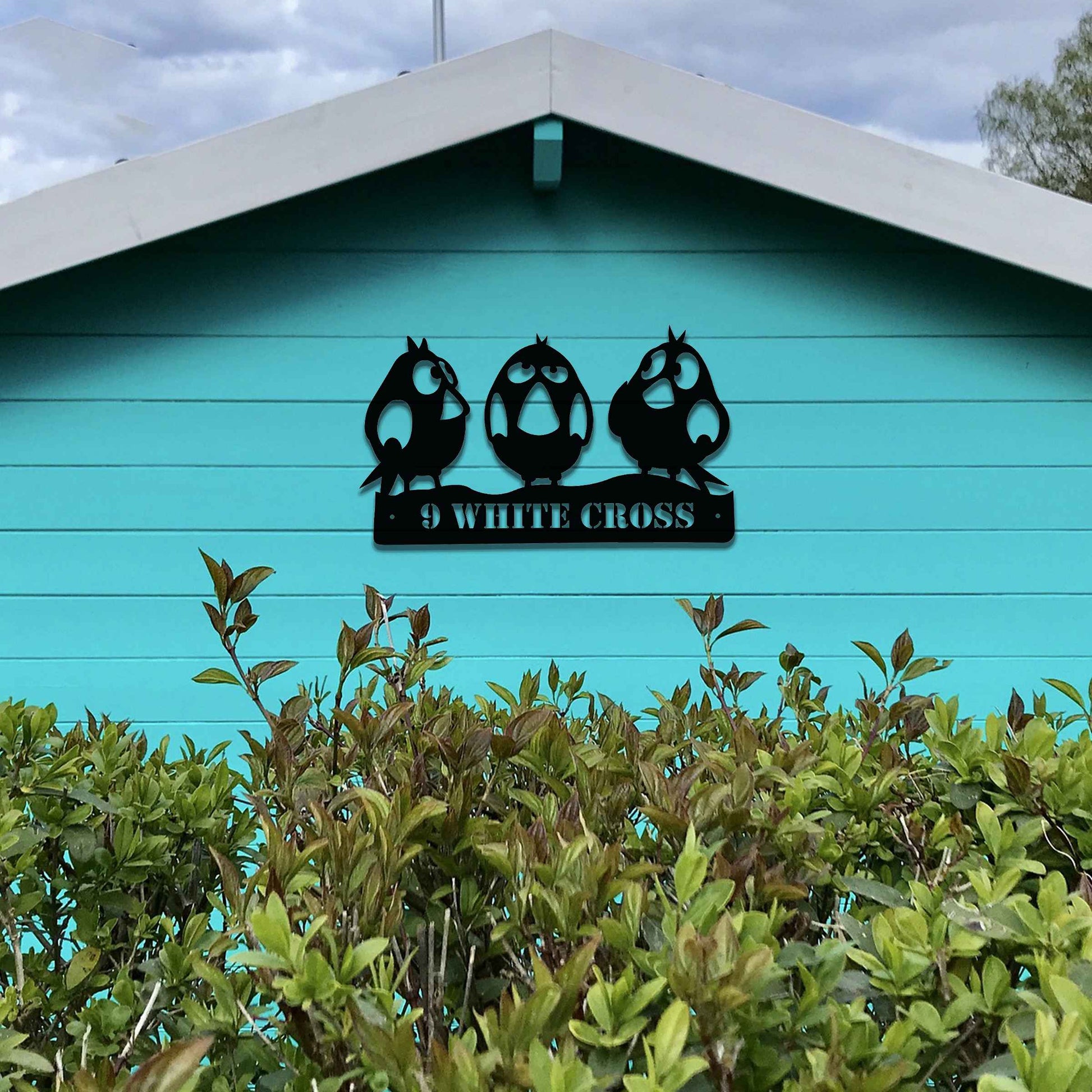 Metal garden decoration featuring three playful bird silhouettes perched on a customisable nameplate, adding a personalised and charming touch to outdoor walls, fences, or sheds.