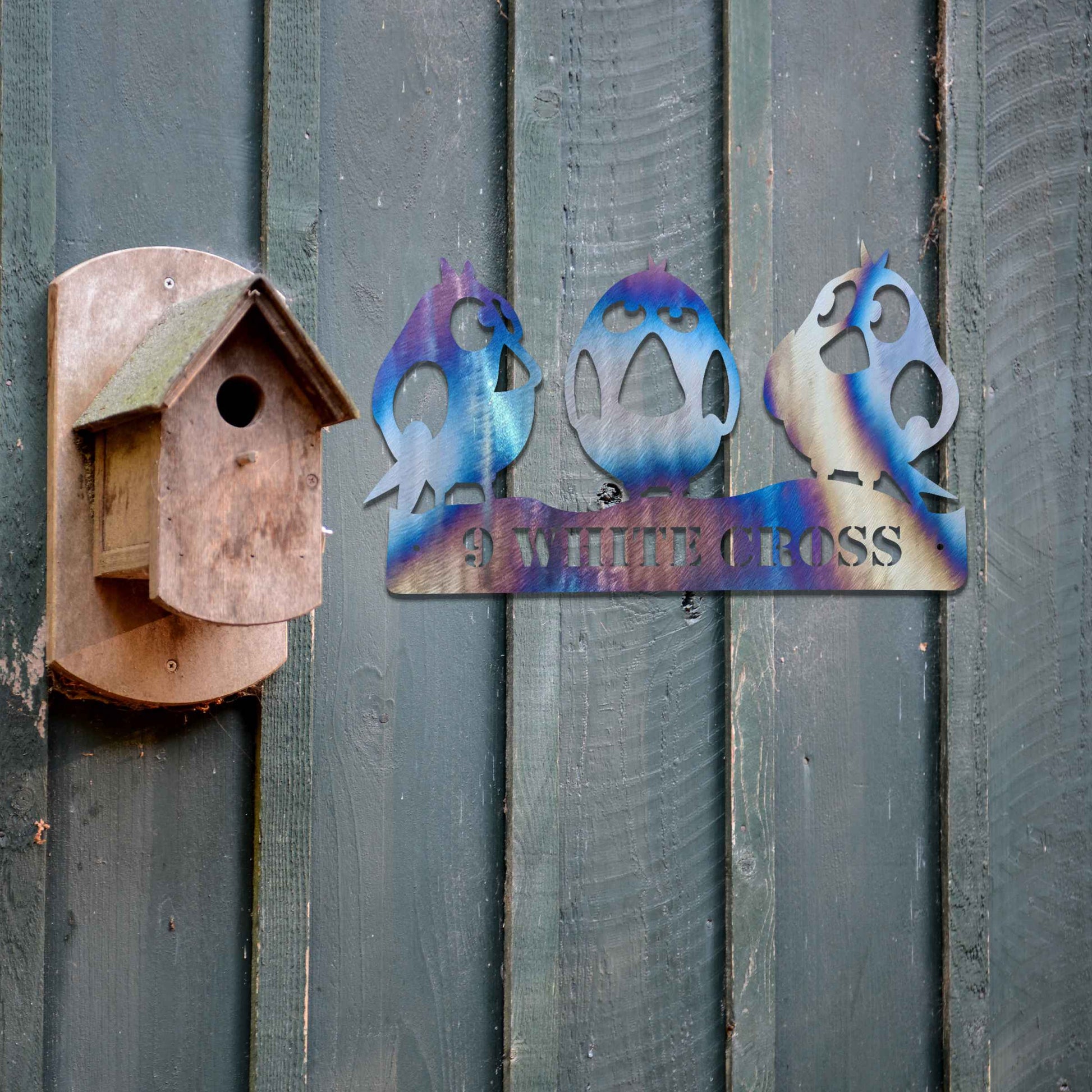 Metal garden decoration featuring three playful bird silhouettes perched on a customisable nameplate, adding a personalised and charming touch to outdoor walls, fences, or sheds.