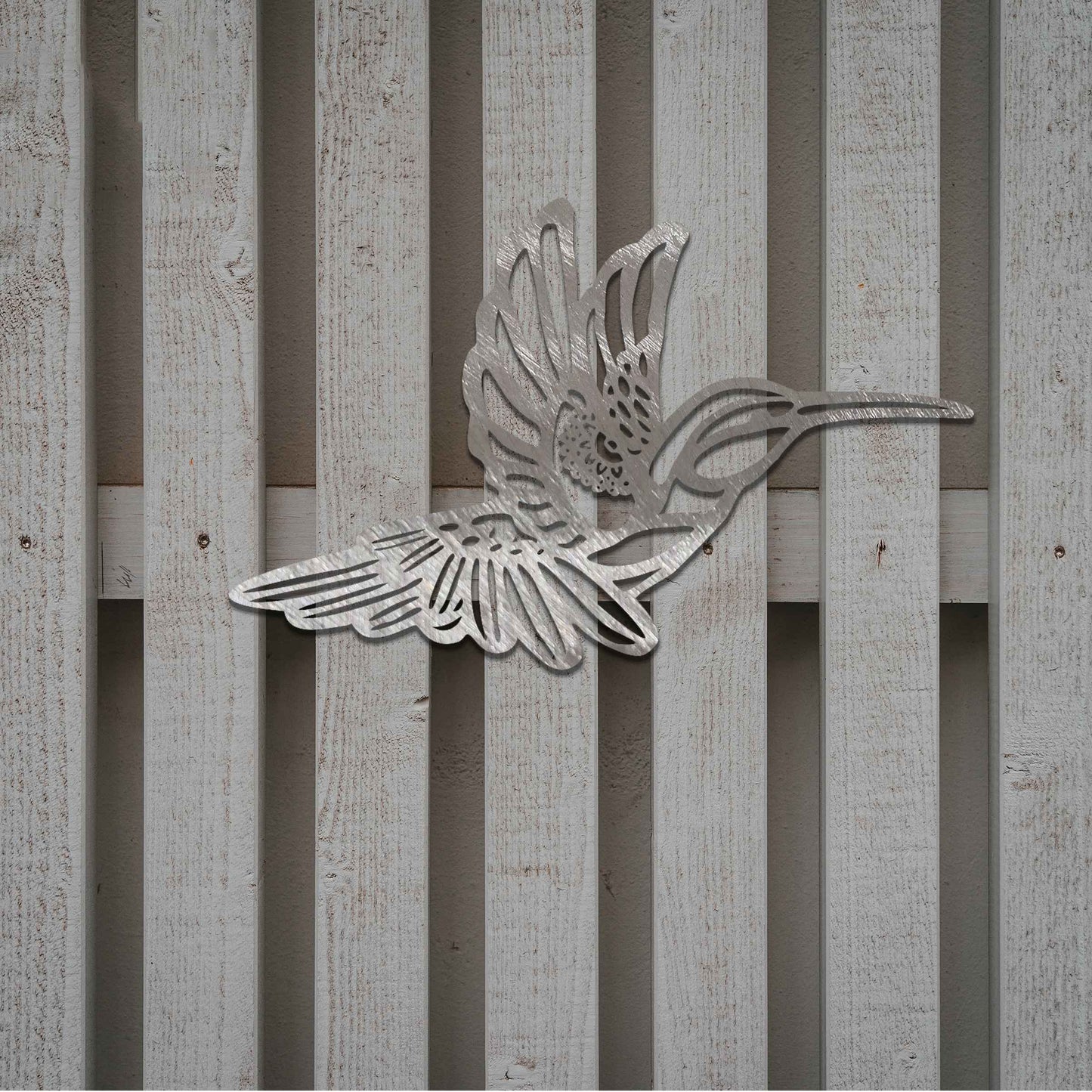 Metal garden decoration featuring a hummingbird in flight with intricate detailing, showcasing a rustic finish that adds a natural and artistic charm to outdoor walls or garden settings.