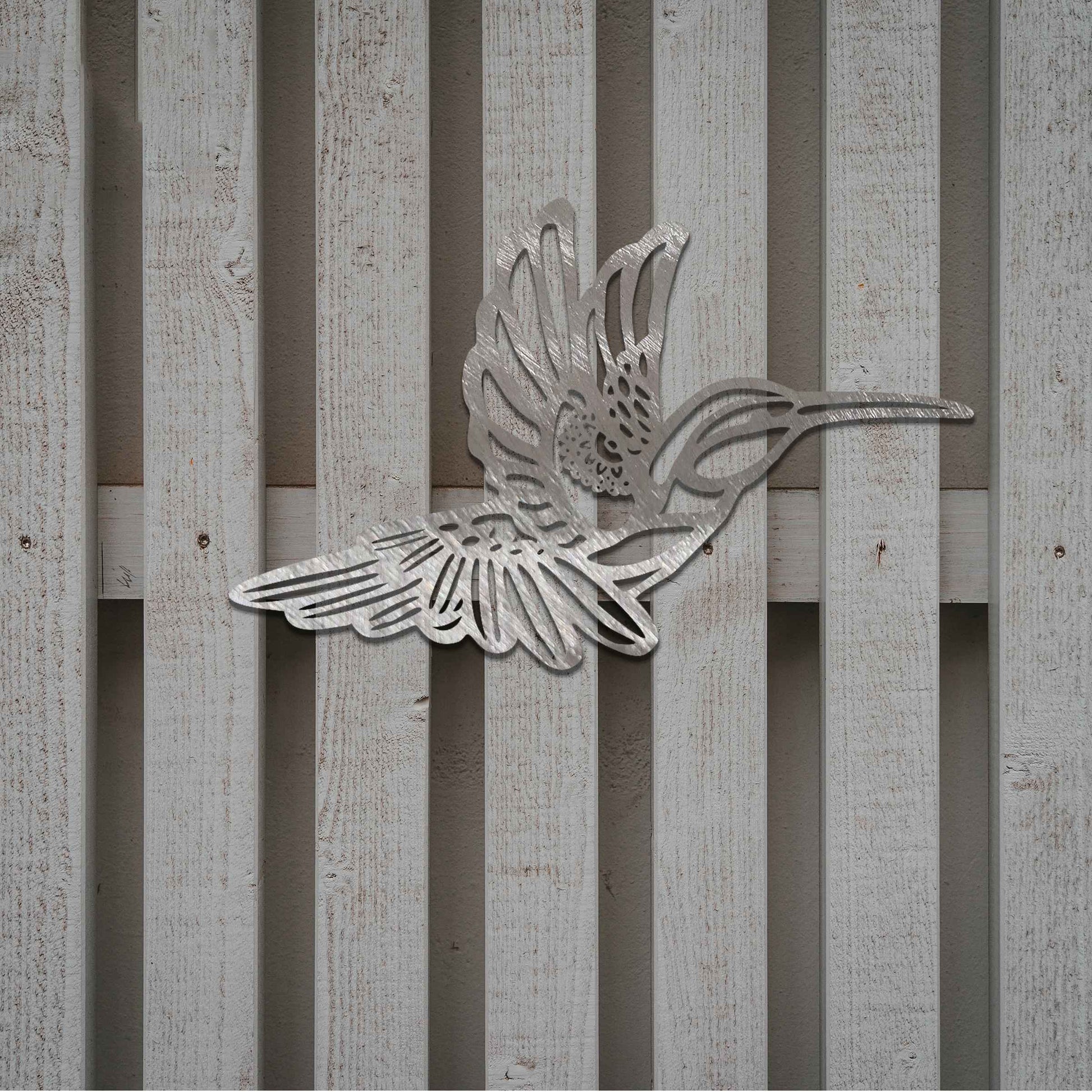 Metal garden decoration featuring a hummingbird in flight with intricate detailing, showcasing a rustic finish that adds a natural and artistic charm to outdoor walls or garden settings.