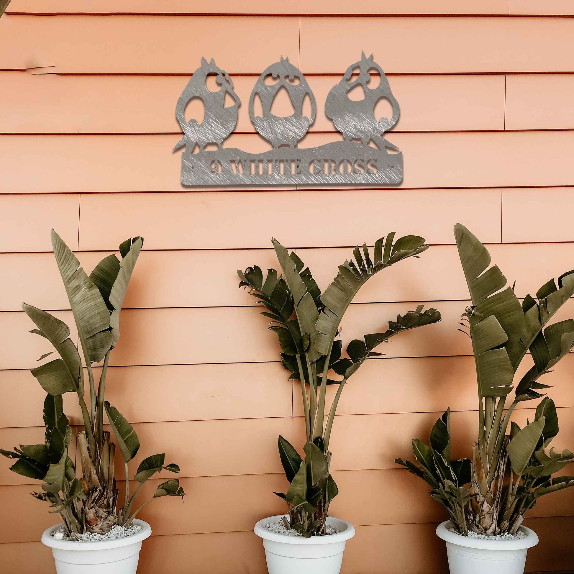 Metal garden decoration featuring three playful bird silhouettes perched on a customisable nameplate, adding a personalised and charming touch to outdoor walls, fences, or sheds.