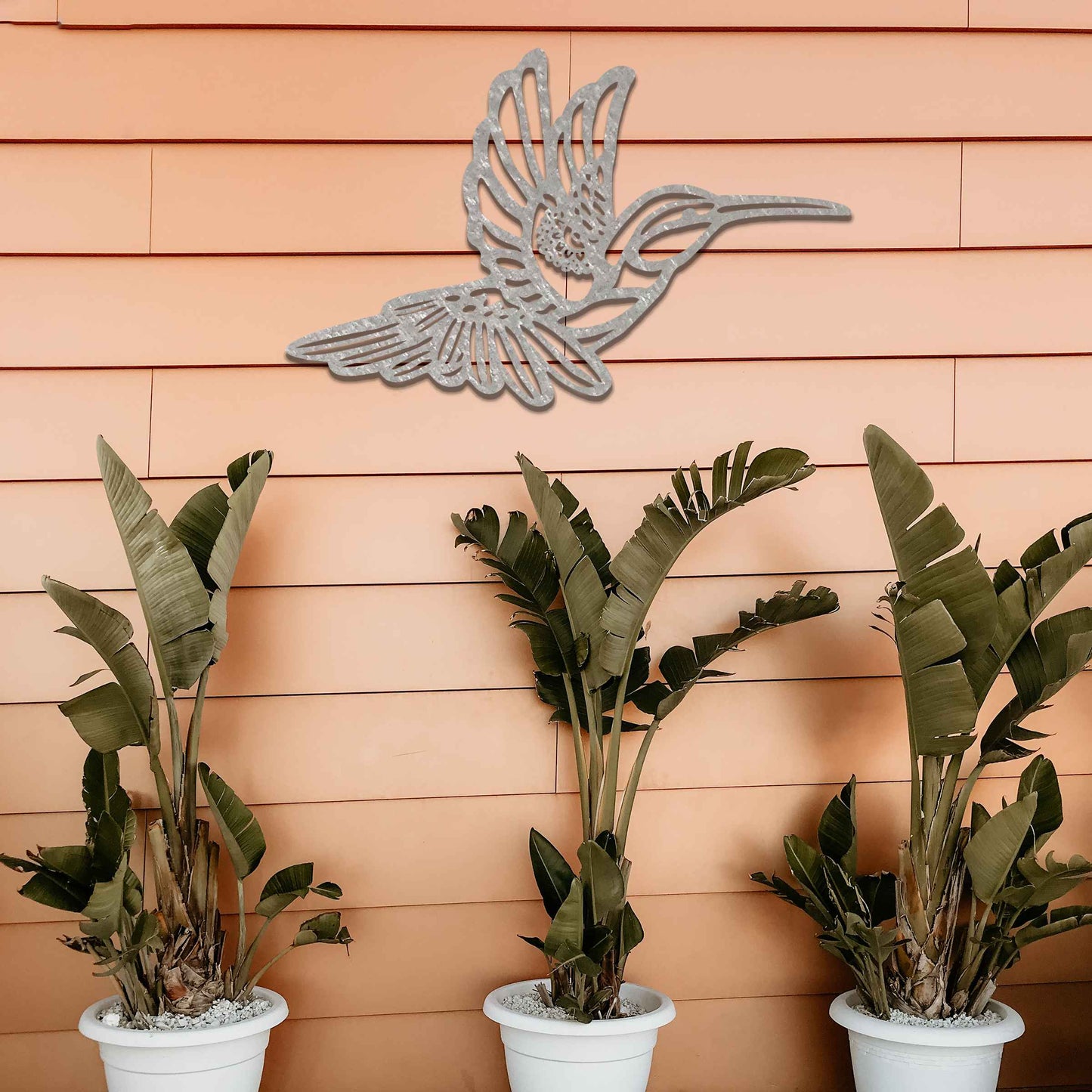 Metal garden decoration featuring a hummingbird in flight with intricate detailing, showcasing a rustic finish that adds a natural and artistic charm to outdoor walls or garden settings.
