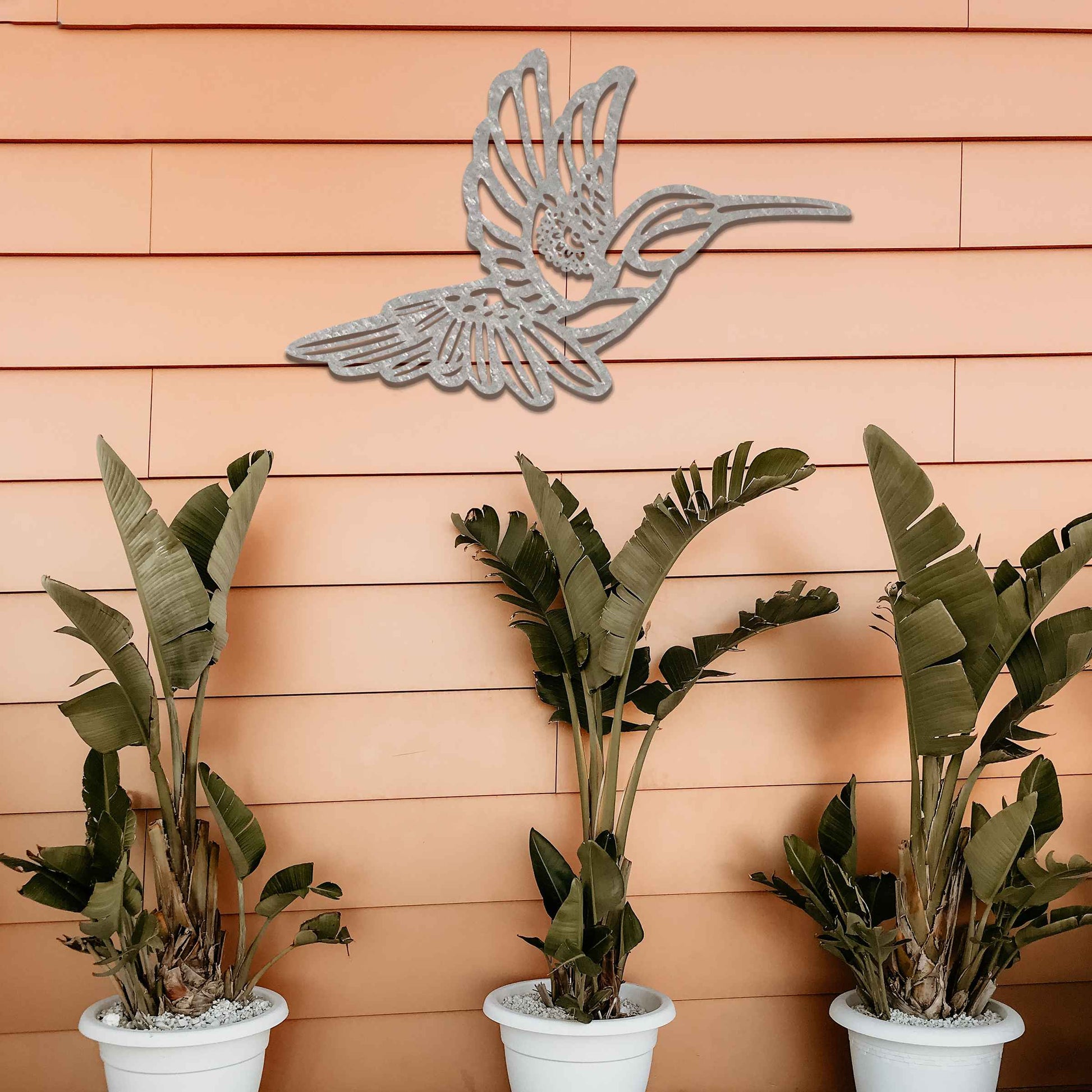 Metal garden decoration featuring a hummingbird in flight with intricate detailing, showcasing a rustic finish that adds a natural and artistic charm to outdoor walls or garden settings.