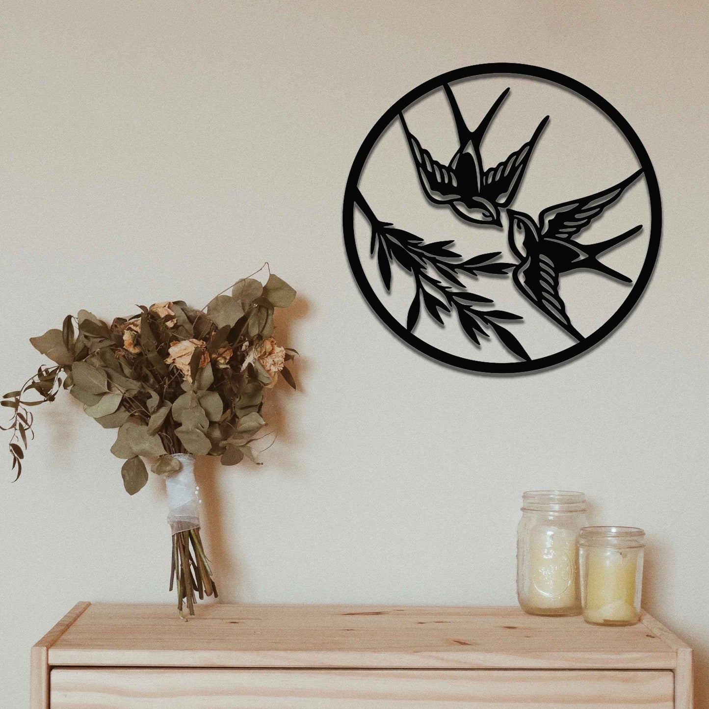 Metal garden decoration featuring two swallows in flight within a circular frame, accented by delicate branch details, combining nature-inspired elegance and craftsmanship to enhance outdoor or indoor spaces.