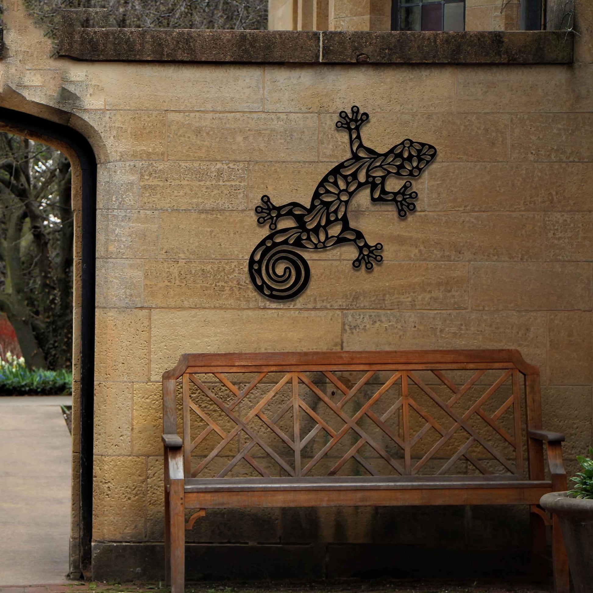 Metal garden decoration featuring a gecko design with floral and spiral cutouts, offering a playful and artistic accent to outdoor walls, seamlessly blending into rustic and natural settings.