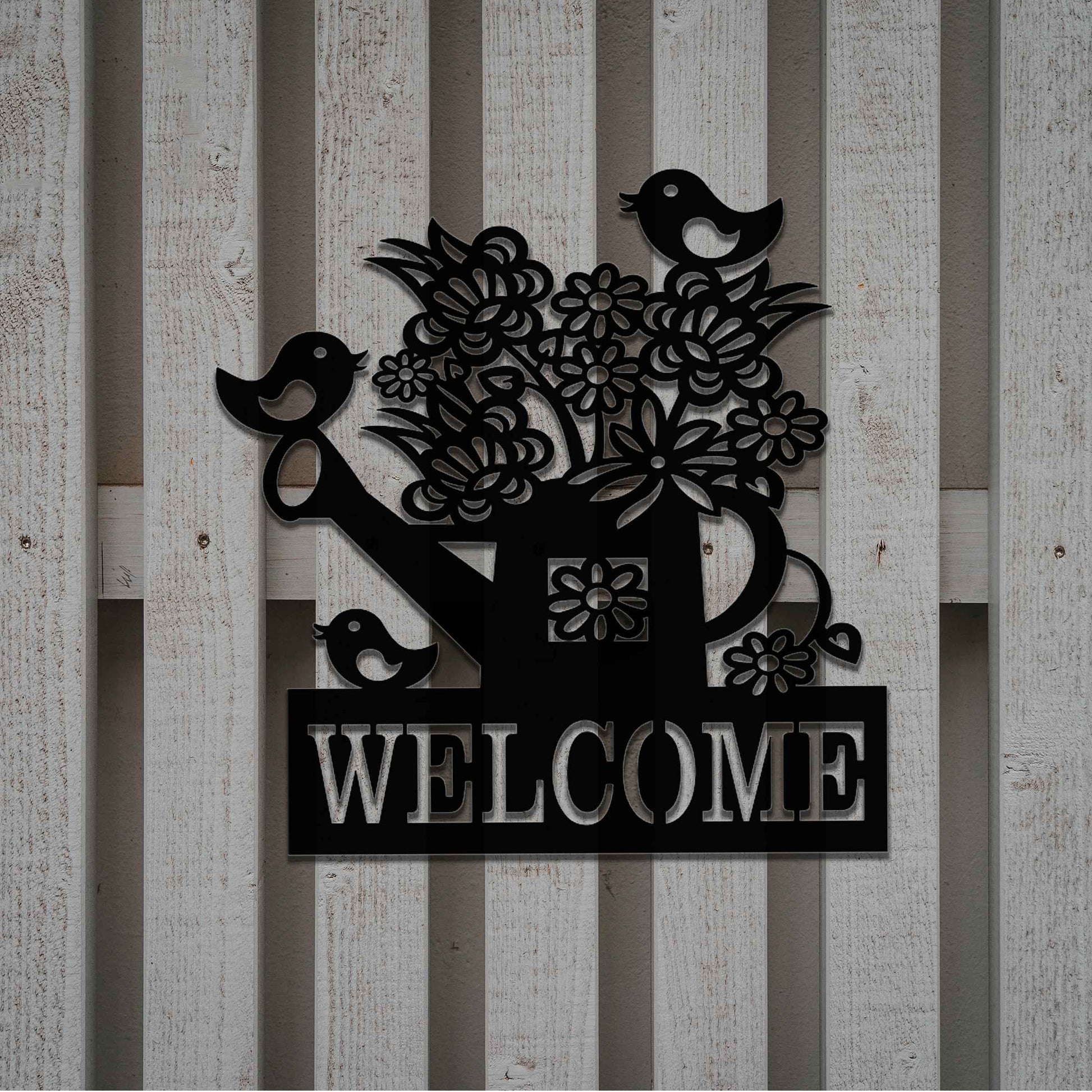 Metal wall decoration featuring a watering can filled with flowers, birds perched on its handle, and the word "WELCOME" displayed below, crafted with intricate cutouts and a rustic finish, adding a warm and inviting touch to indoor or outdoor spaces.