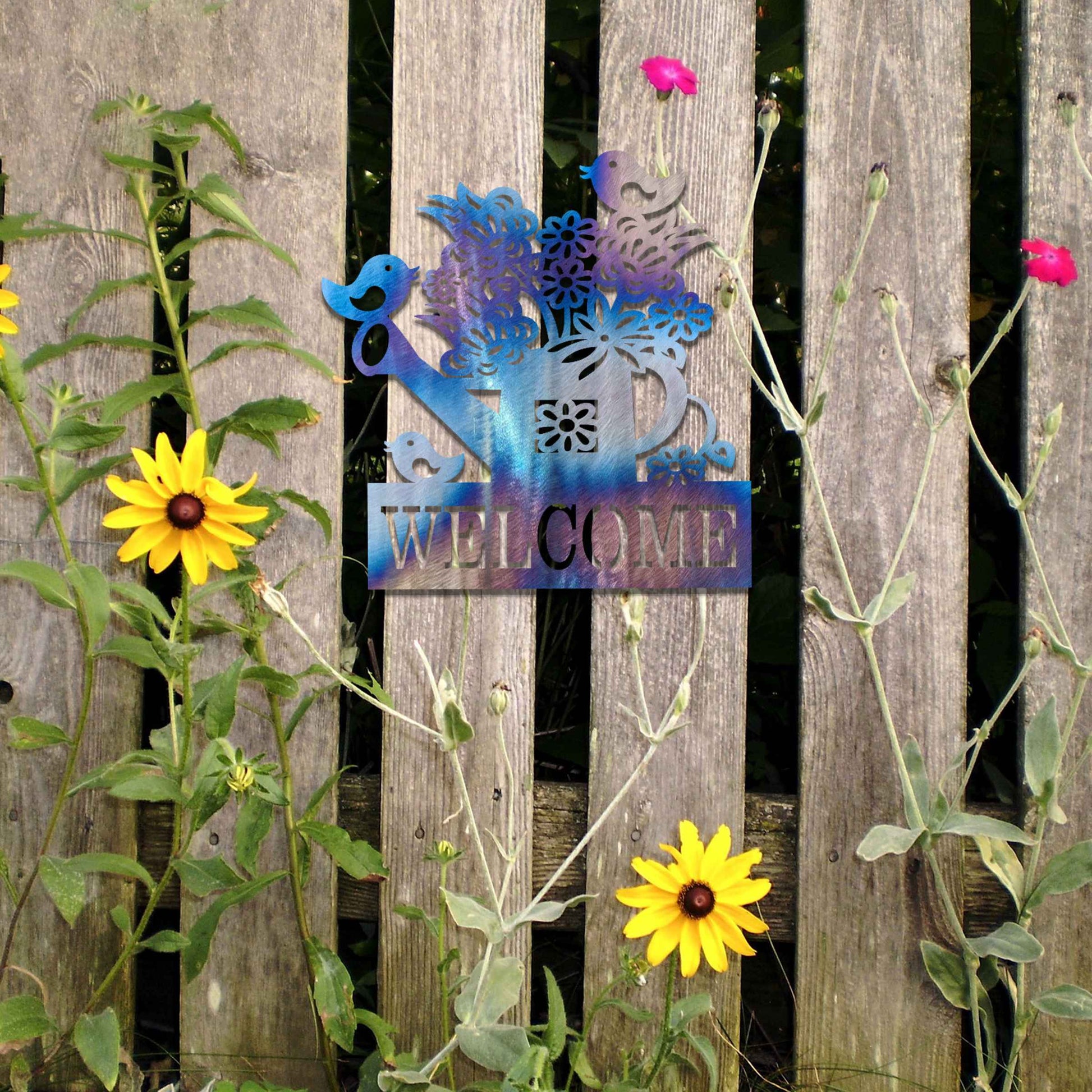 Metal wall decoration featuring a watering can filled with flowers, birds perched on its handle, and the word "WELCOME" displayed below, crafted with intricate cutouts and a rustic finish, adding a warm and inviting touch to indoor or outdoor spaces.