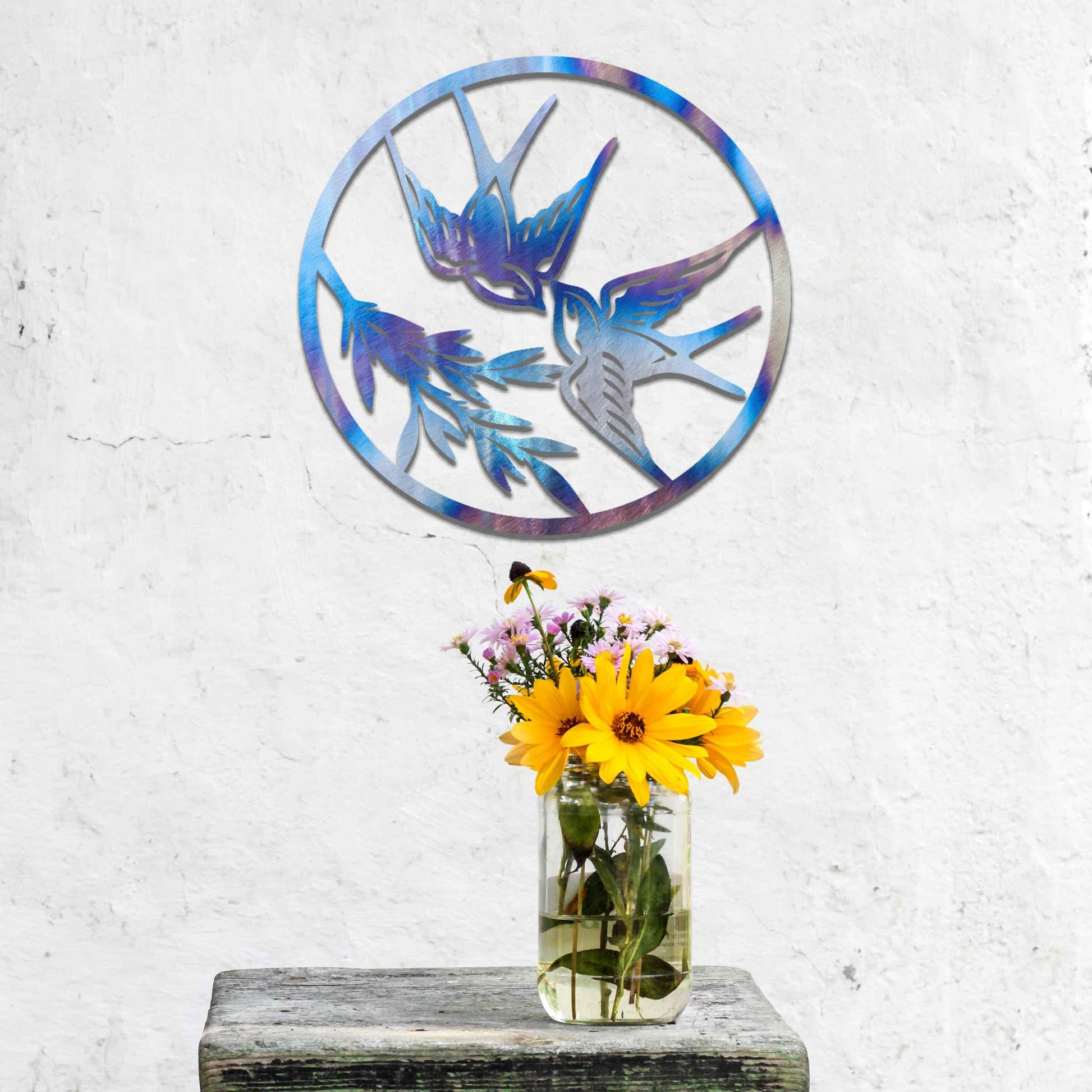 Metal garden decoration featuring two swallows in flight within a circular frame, accented by delicate branch details, combining nature-inspired elegance and craftsmanship to enhance outdoor or indoor spaces.