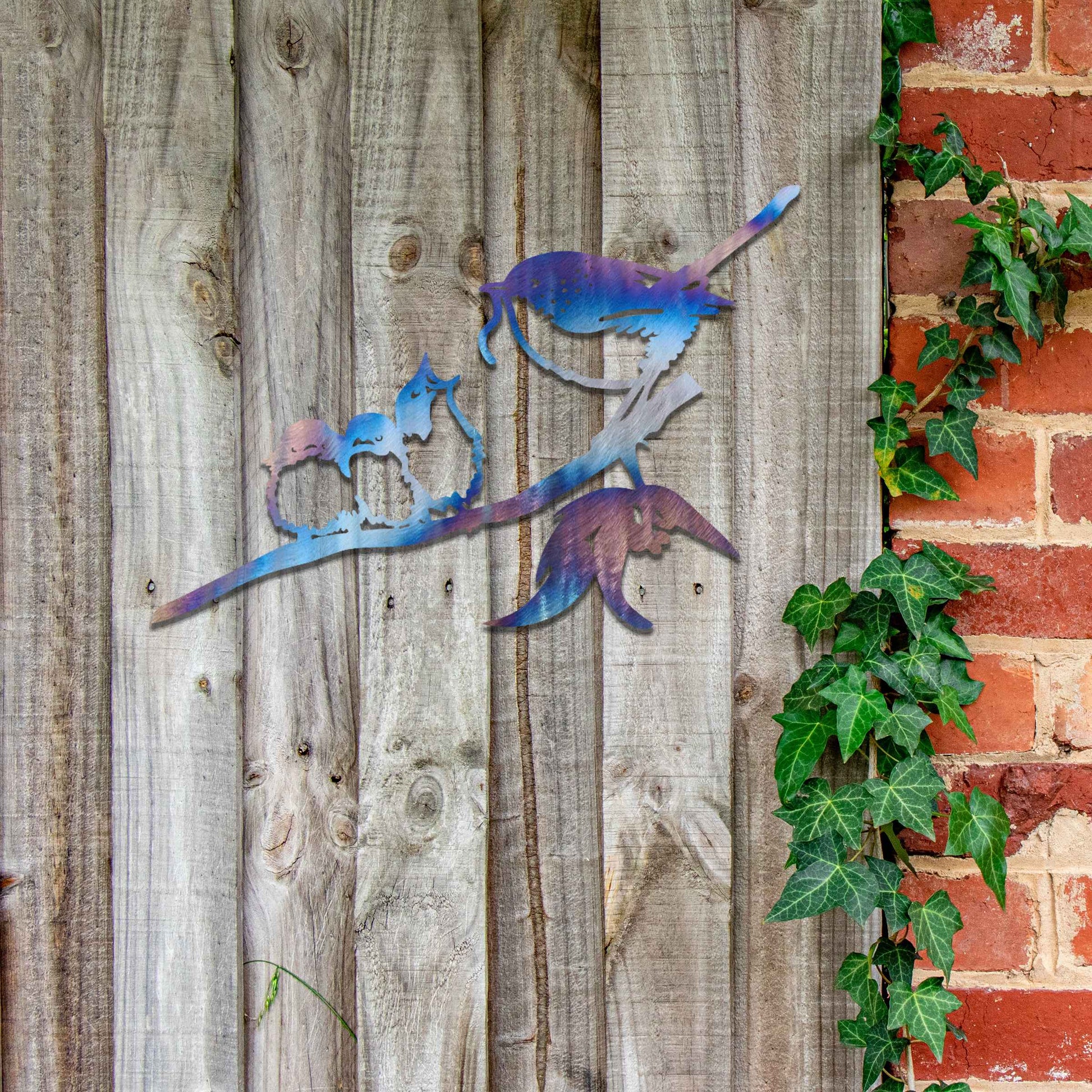 Metal wall art featuring a bird perched on a branch with two smaller birds sitting closely together, crafted in a rustic finish. This piece brings a touch of nature-inspired charm to indoor or outdoor spaces.