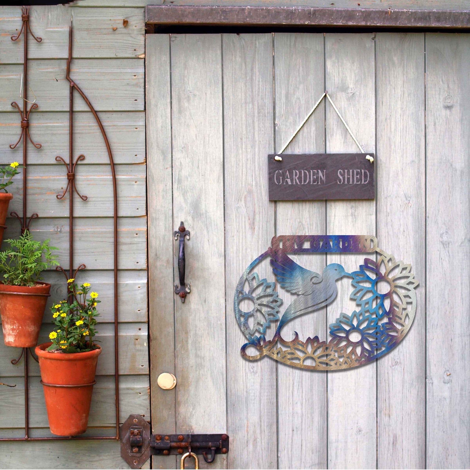 Metal garden decoration featuring a hummingbird surrounded by blooming sunflowers within an oval frame, inscribed with "My Garden," adding a personalised and nature-inspired charm to outdoor walls or fences.