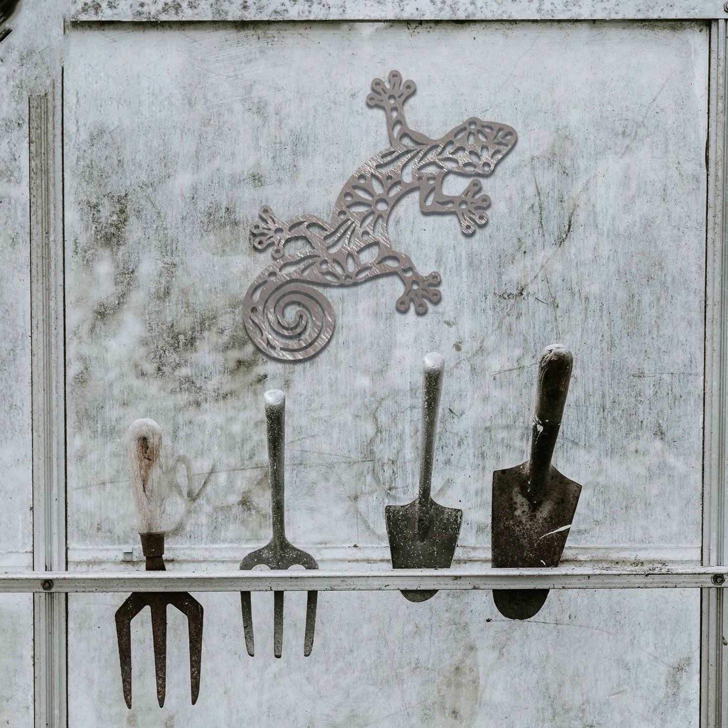 Metal garden decoration featuring a gecko design with floral and spiral cutouts, offering a playful and artistic accent to outdoor walls, seamlessly blending into rustic and natural settings.