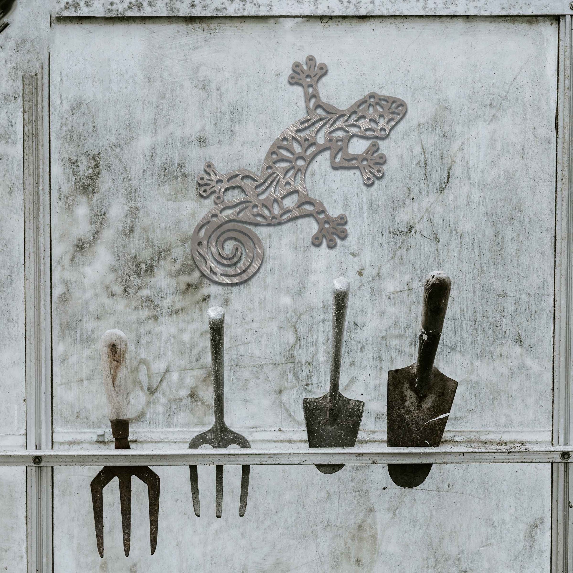 Metal garden decoration featuring a gecko design with floral and spiral cutouts, offering a playful and artistic accent to outdoor walls, seamlessly blending into rustic and natural settings.