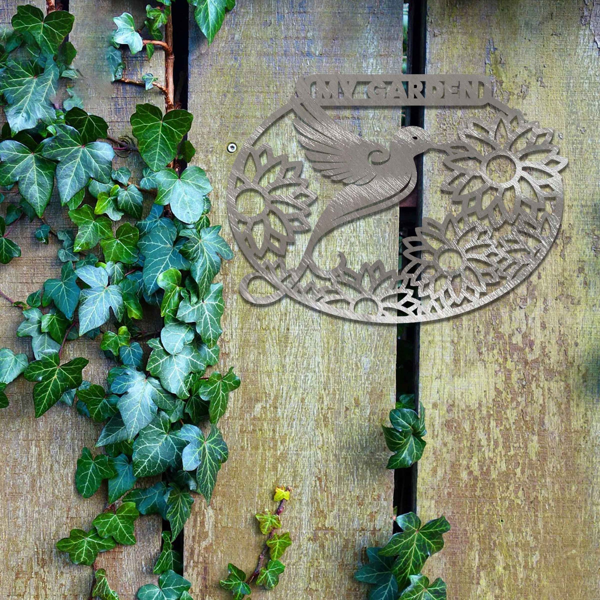 Metal garden decoration featuring a hummingbird surrounded by blooming sunflowers within an oval frame, inscribed with "My Garden," adding a personalised and nature-inspired charm to outdoor walls or fences.