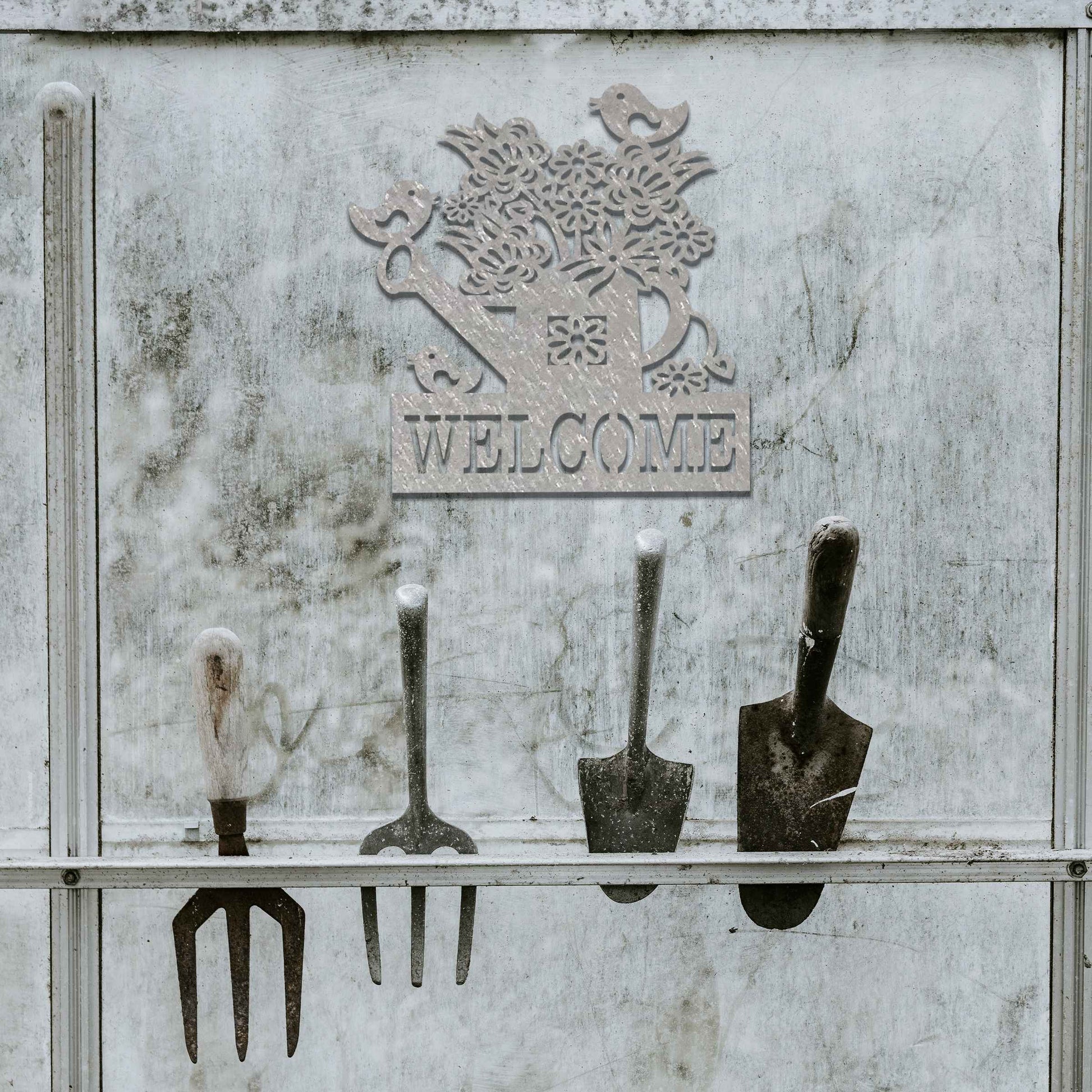Metal wall decoration featuring a watering can filled with flowers, birds perched on its handle, and the word "WELCOME" displayed below, crafted with intricate cutouts and a rustic finish, adding a warm and inviting touch to indoor or outdoor spaces.