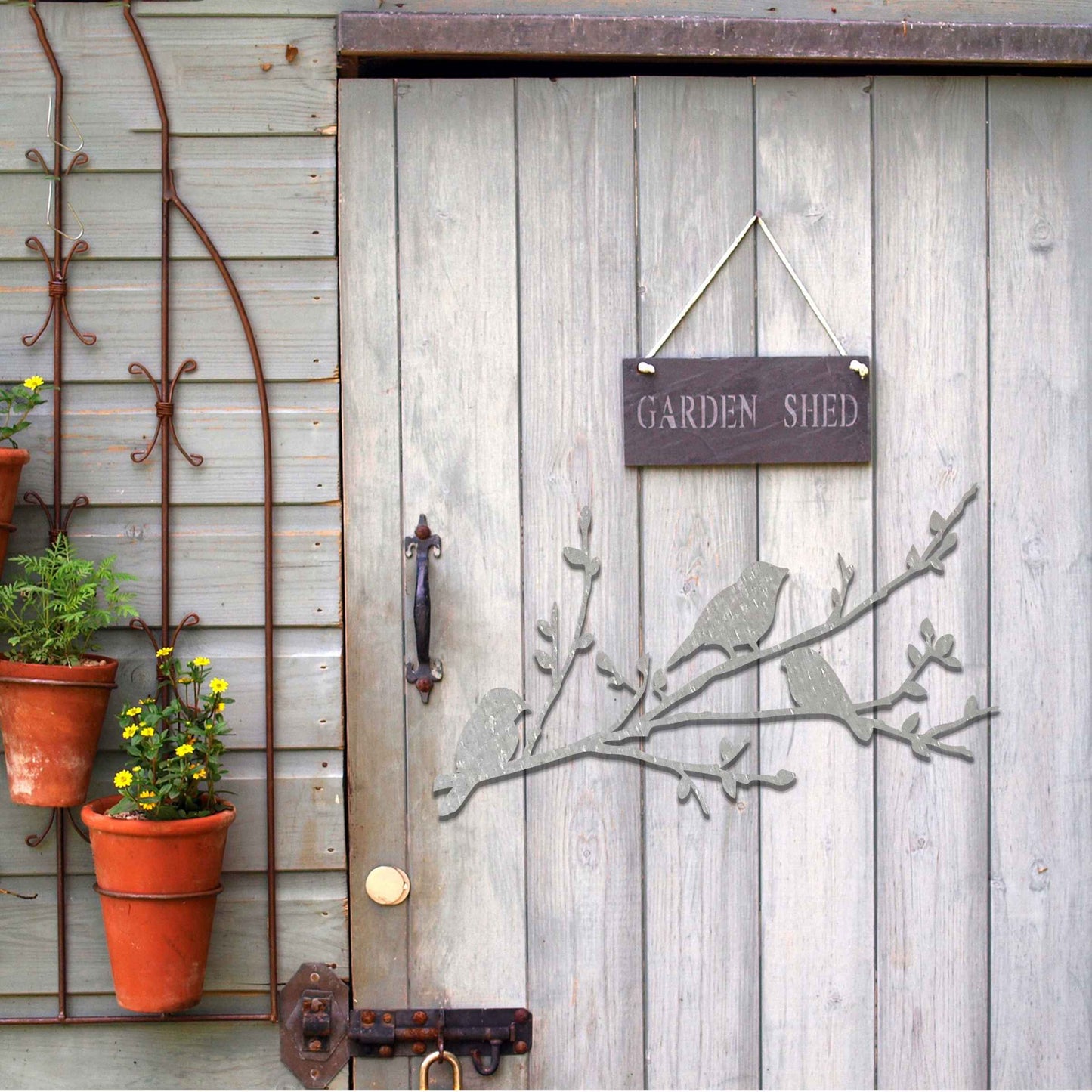Metal garden decoration featuring three birds perched on a leafy branch, crafted with intricate cutout details and a rustic finish, adding a charming and natural touch to outdoor walls or garden spaces.