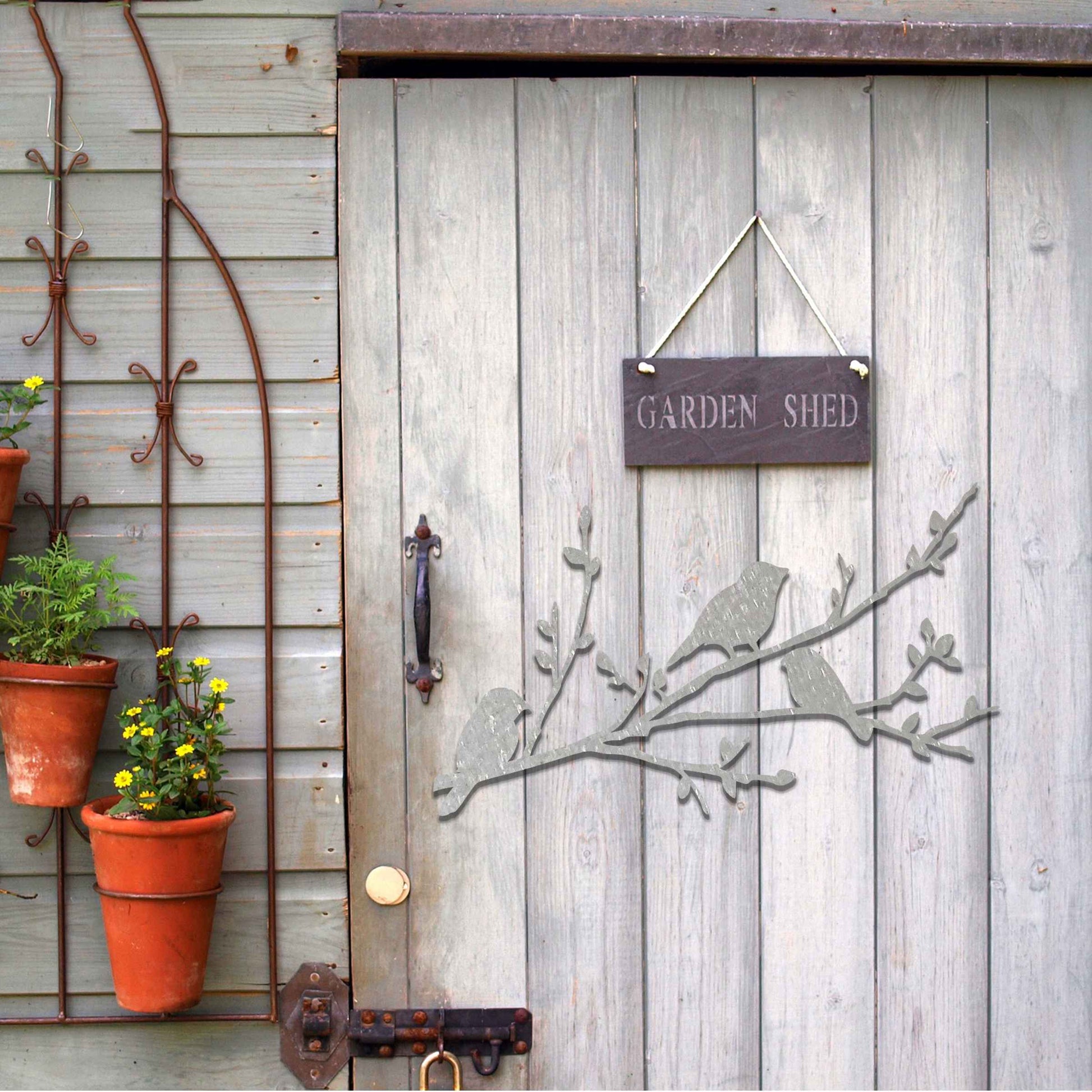 Metal garden decoration featuring three birds perched on a leafy branch, crafted with intricate cutout details and a rustic finish, adding a charming and natural touch to outdoor walls or garden spaces.