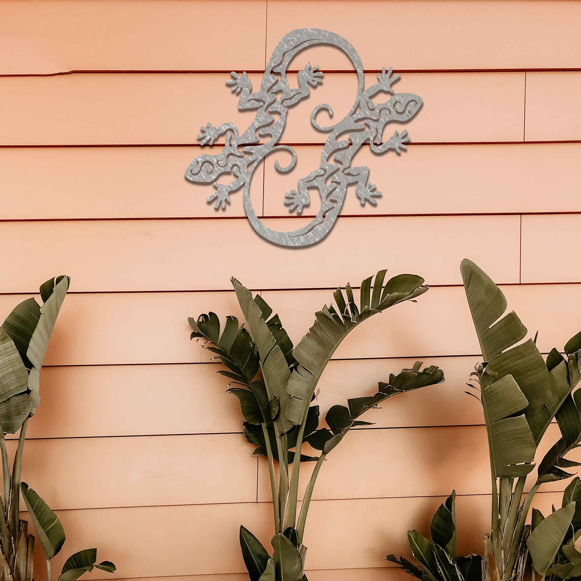 Metal wall decoration featuring two intertwined gecko designs with flowing and curved patterns, adding a dynamic and modern artistic touch to indoor spaces, displayed on a neutral wall within contemporary decor.