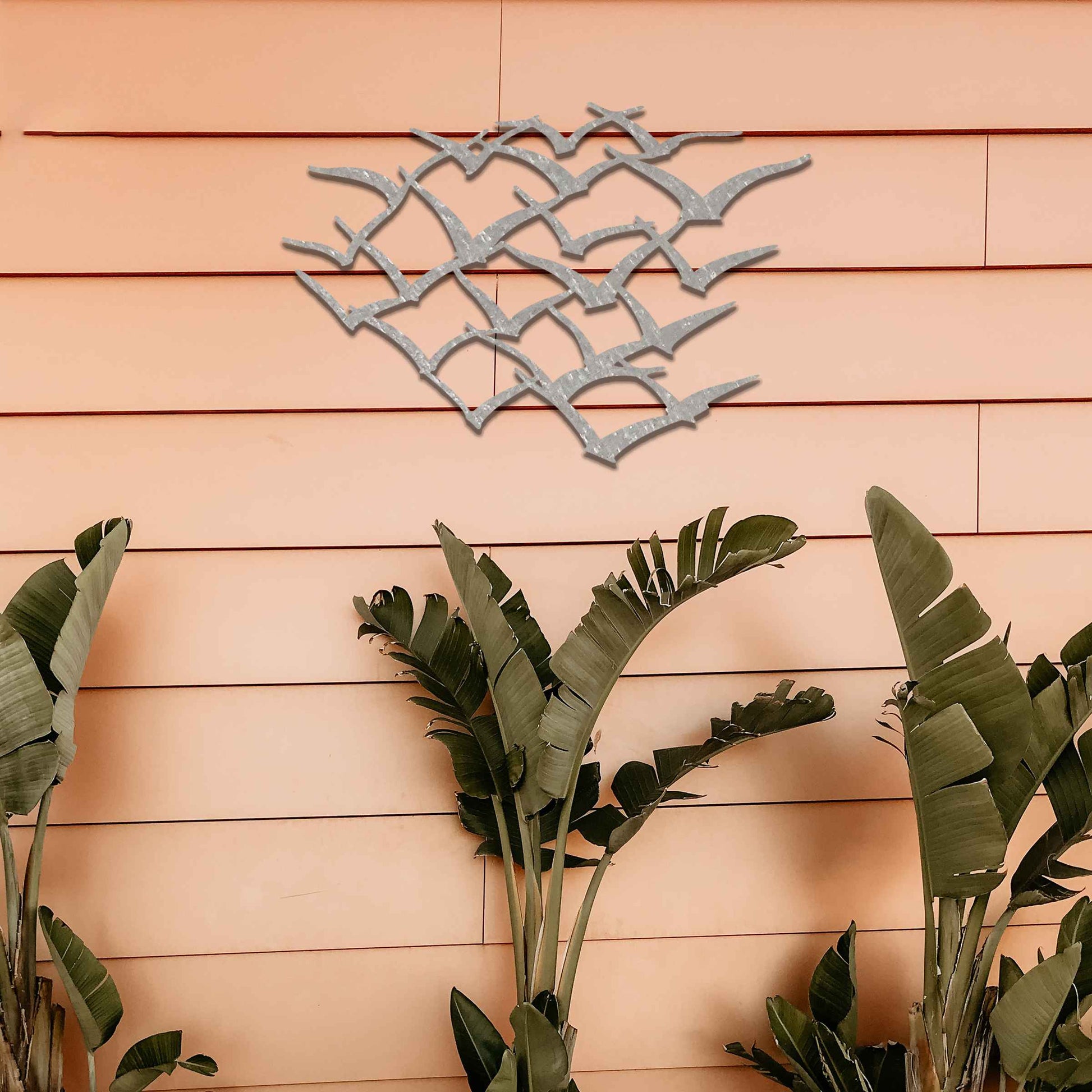 A stunning metal wall art featuring an abstract flock of birds in flight. This dynamic piece brings an element of freedom and movement to your space, complementing lush green surroundings for a serene and modern aesthetic.